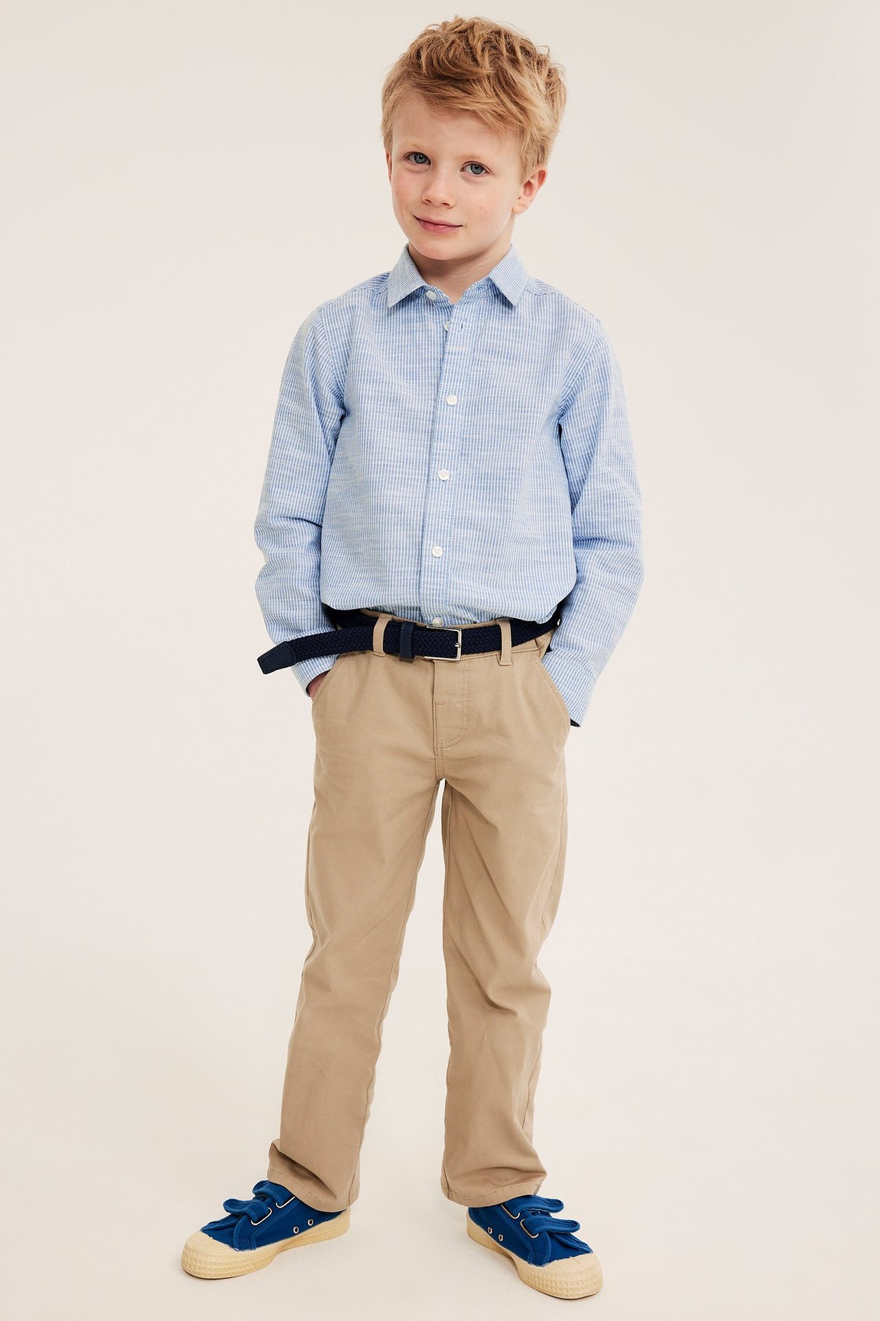 Edestä: Lapsi vaaleansininen raidallinen puuvillapaita, khakihousut, tummansininen vyö, siniset kengät.