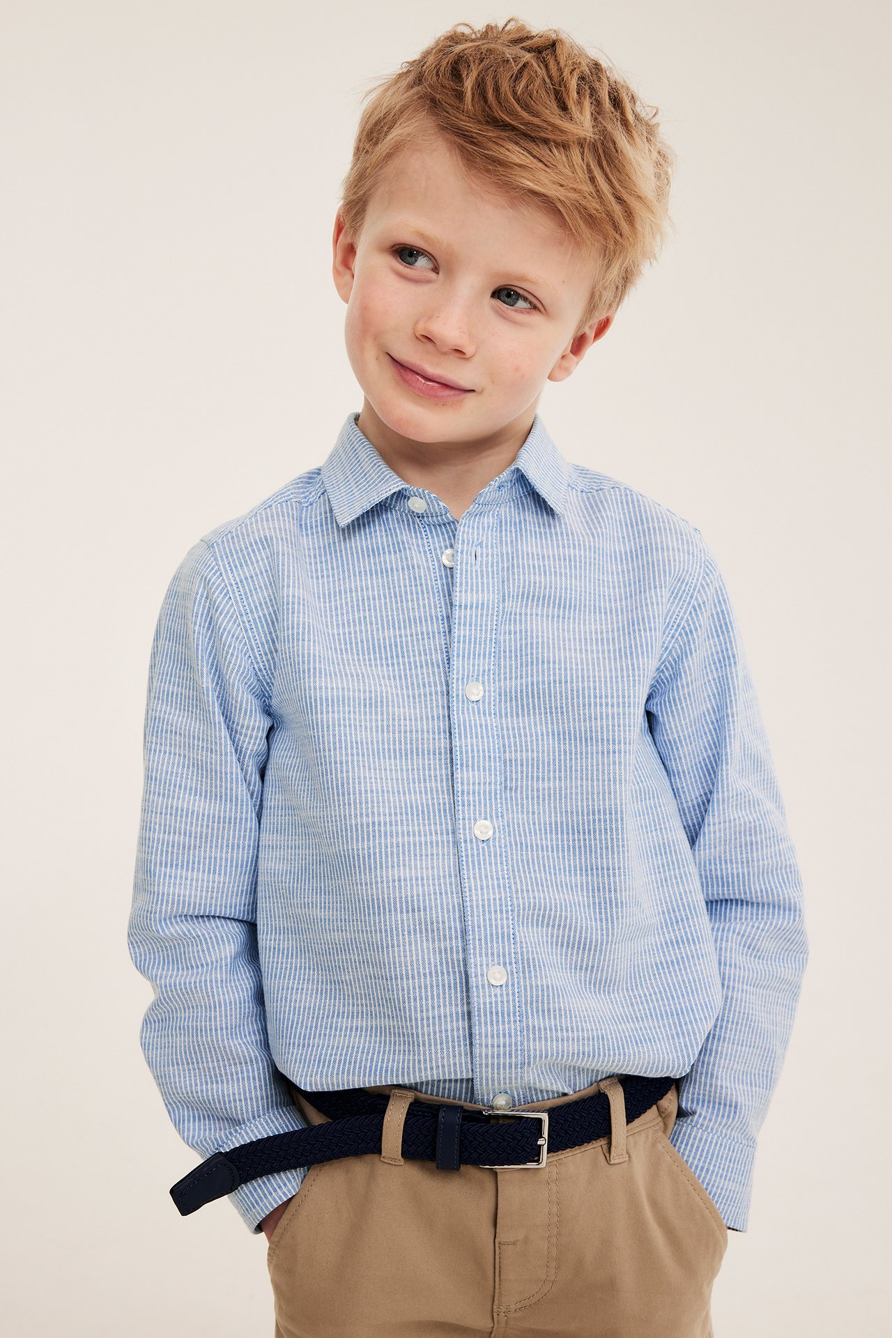 Widok z przodu: Dziecko w jasnoniebieskiej bawełnianej koszuli w paski, beżowych chinosach i granatowym plecionym pasku.