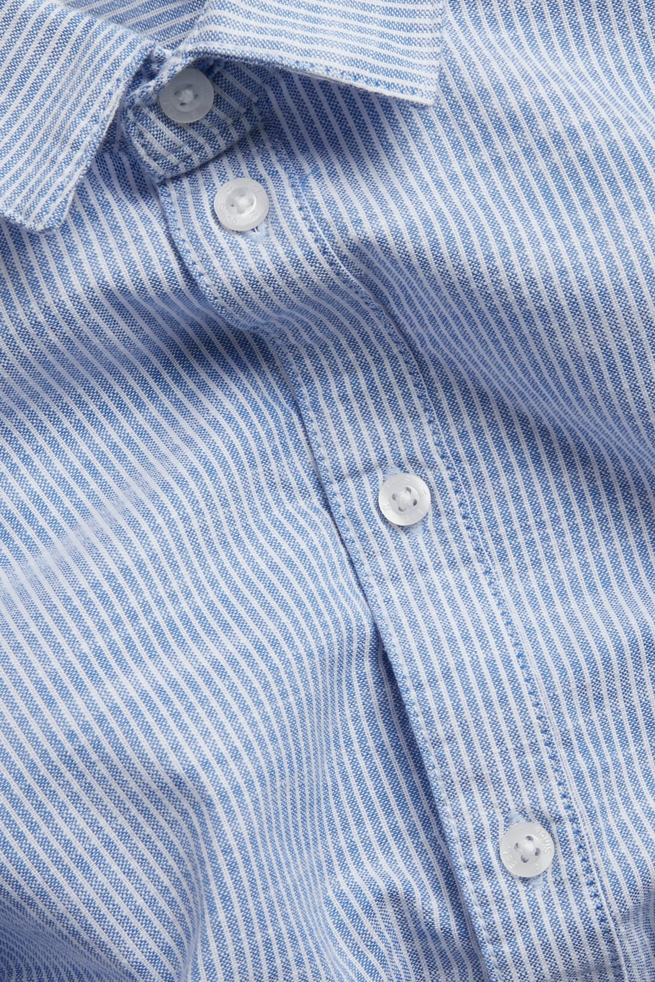 Zbliżenie: dziecięca, bawełniana koszula w jasnoniebieskie i białe paski, z białymi guzikami.