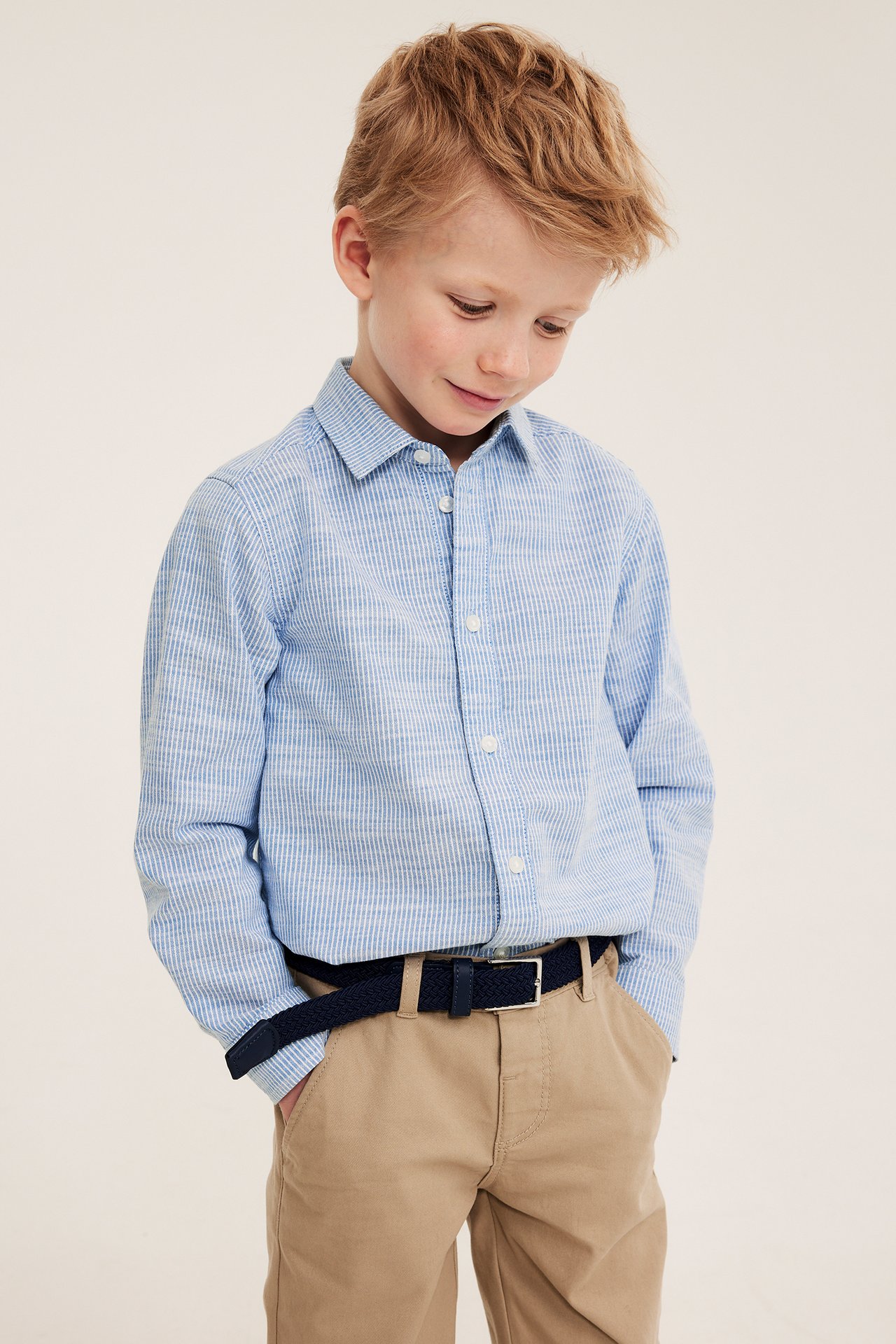 Z przodu: Chłopiec w niebieskiej koszuli w paski, beżowych spodniach i granatowym plecionym pasku.