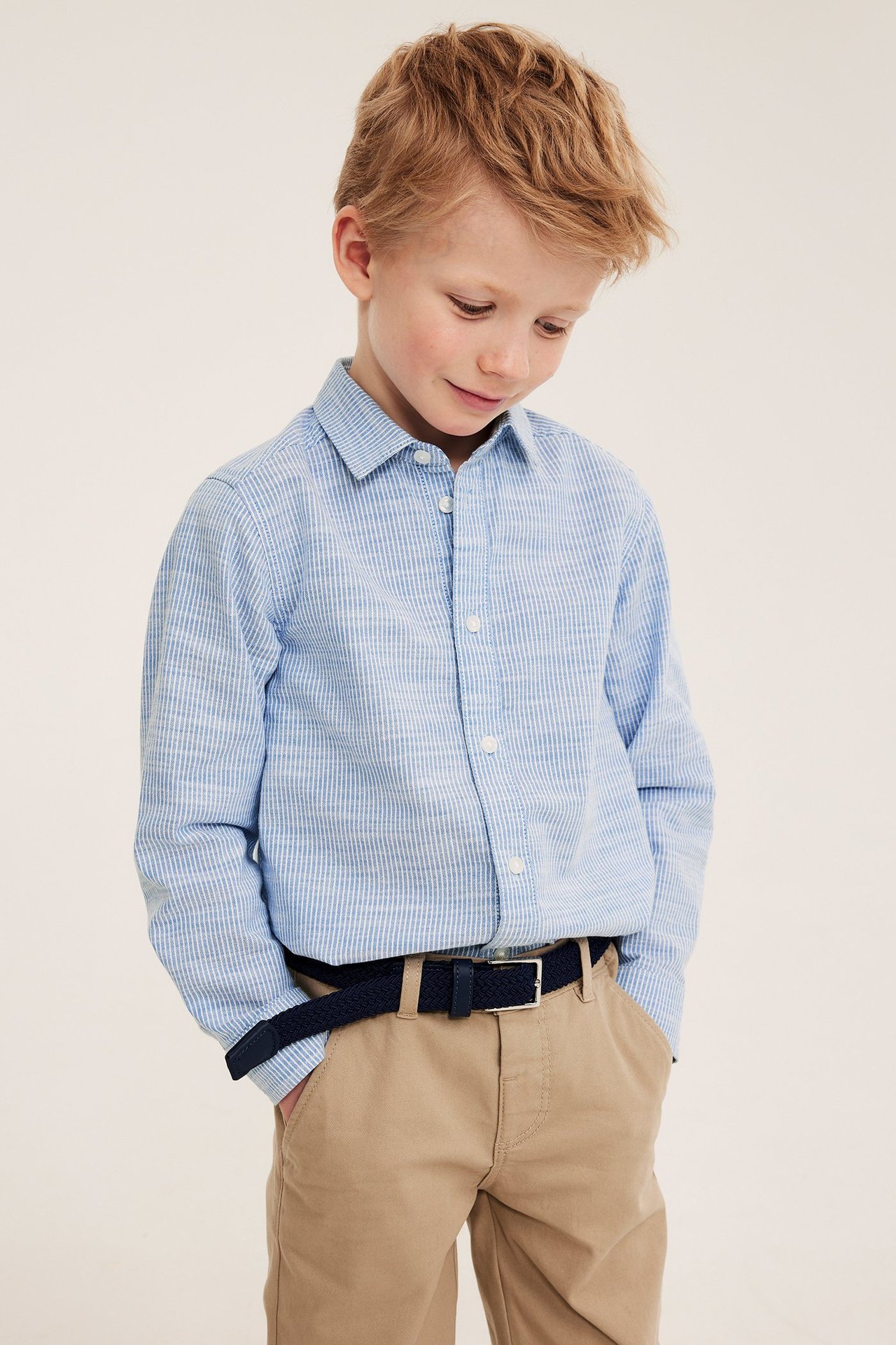 Z przodu: Chłopiec w niebieskiej koszuli w paski, beżowych spodniach i granatowym plecionym pasku.