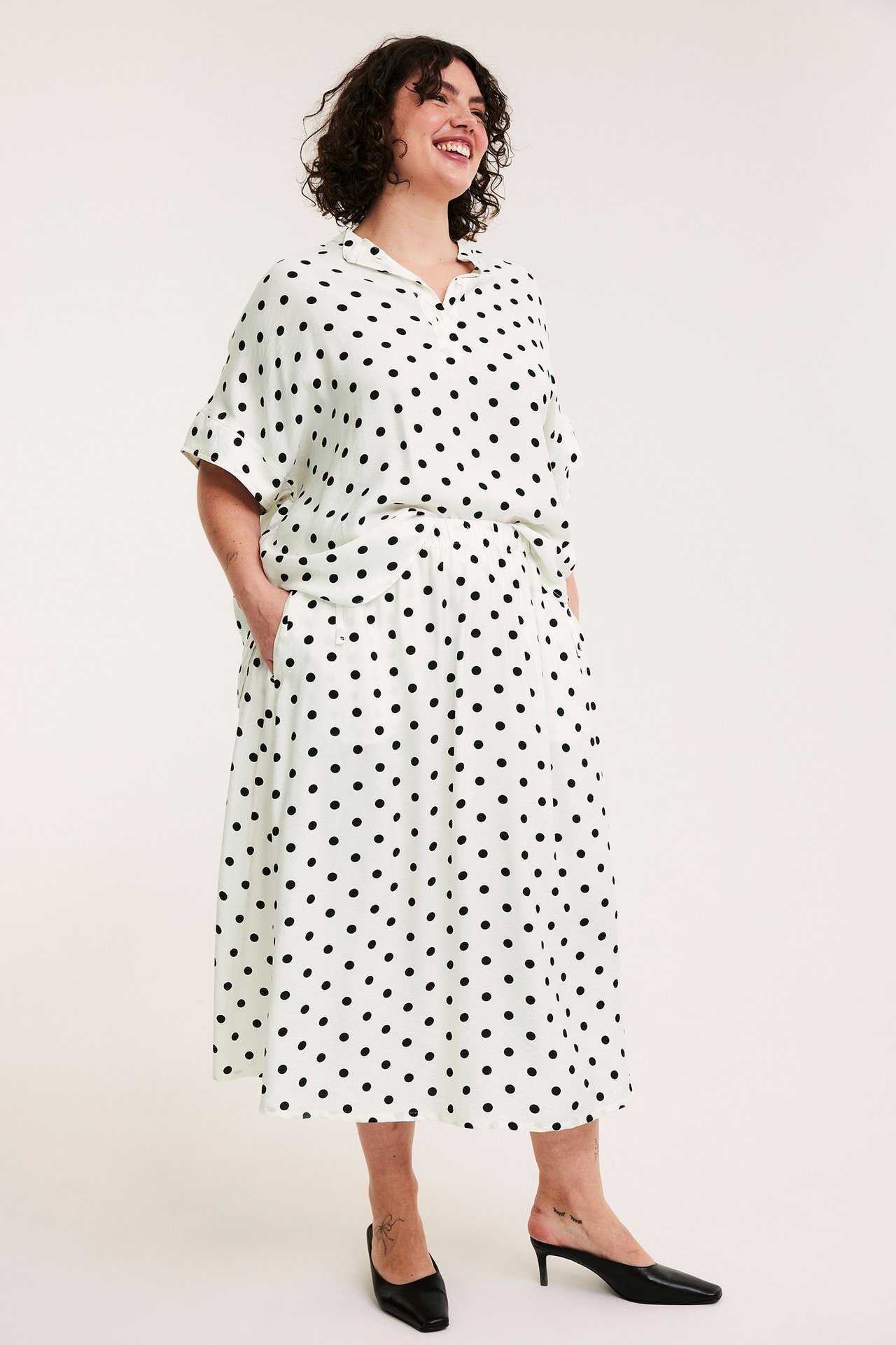 Edestä: Nainen yllään luonnonvalkoinen pitkä pilkkuhame, jossa joustava vyötärö, ja yhteensopiva pusero.