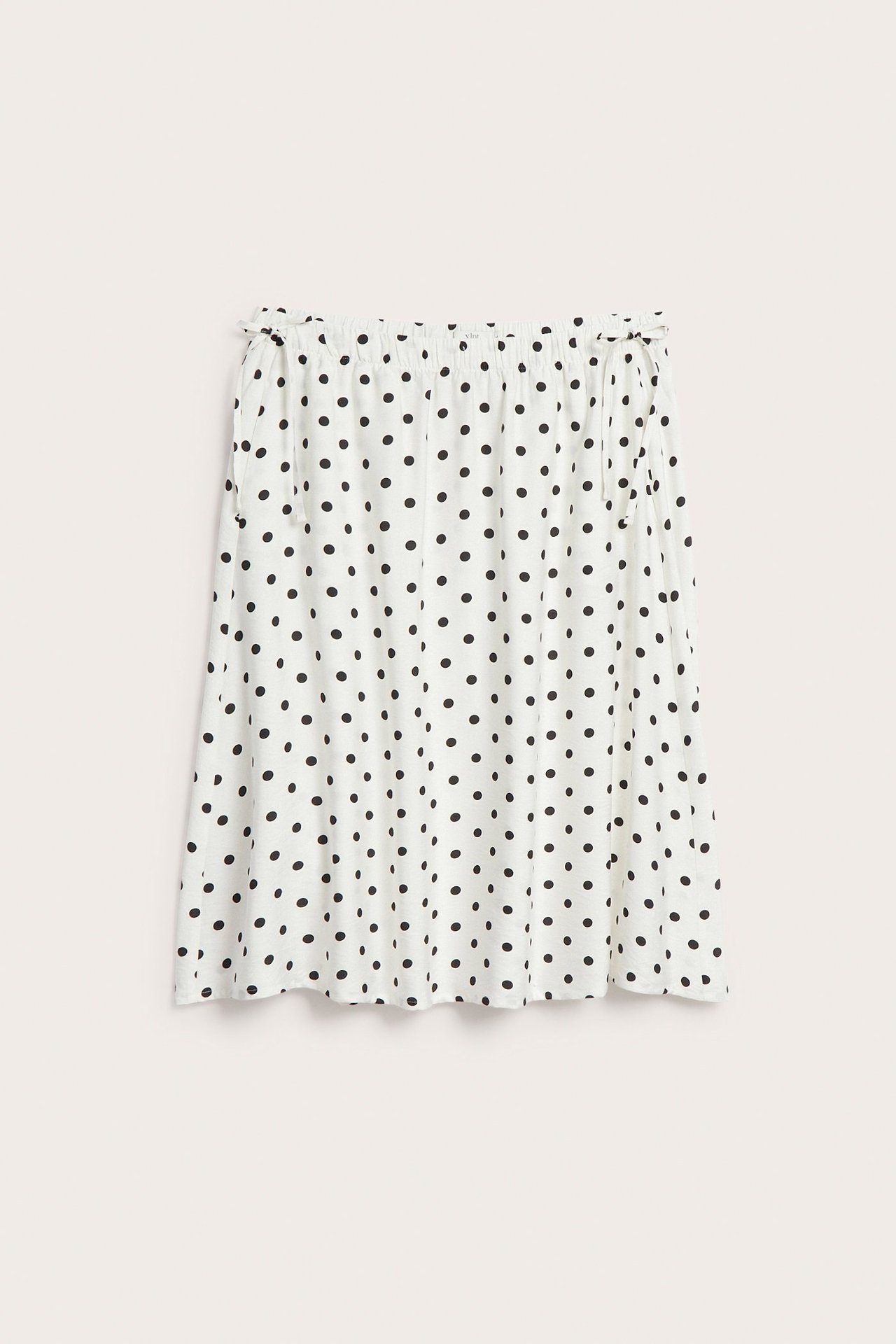 Edestäpäin: Luonnonvalkoinen pitkä popliinihame, jossa mustia pilkkuja, joustovyötärö, nyöritys ja taskut.