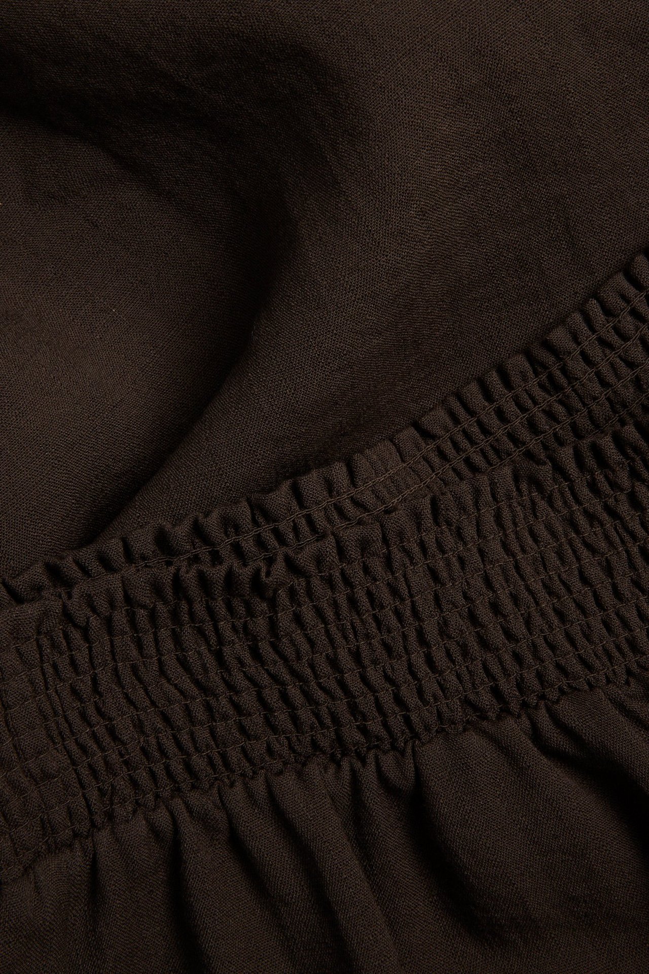 Lähikuva tummanruskeista leveälahkeisista viskoosihousuista, joissa on smokkirypytetty vyötärö.