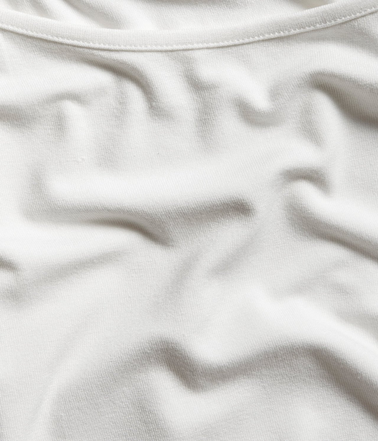 Lähikuva valkoisesta peruspaidasta, näyttäen pehmeän, yksivärisen kankaan ja ribatun pääntien.