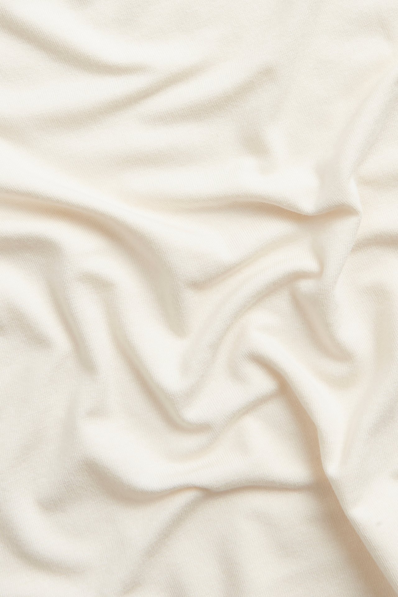 Närbild på mjukt, enfärgat offwhite tyg i viskos-elastan för baslinne med lätta veck.