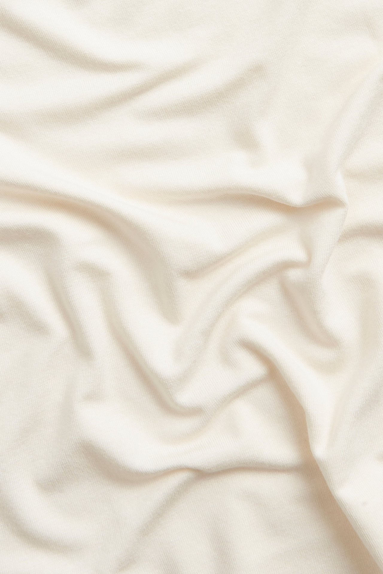 Zbliżenie miękkiego, gładkiego, ecru materiału wiskozowo-elastanowego na top z delikatnymi fałdami.