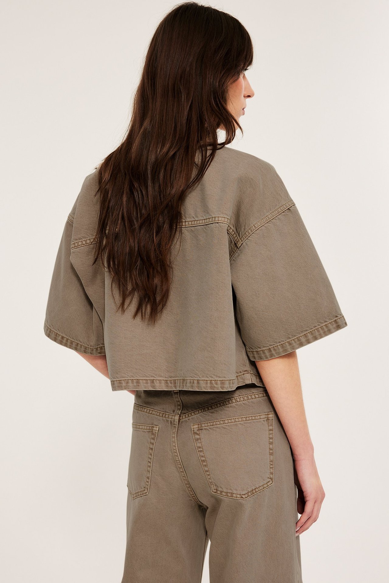 Nainen takaapäin yllään lyhyt khakinvärinen puuvillatvillipaita levein hihoin ja yhteensopivat housut.