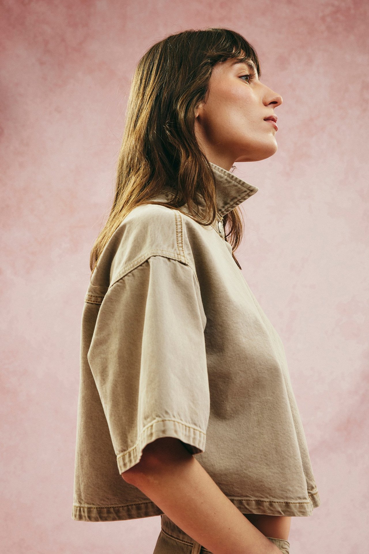 Widok z boku: Kobieta w luźnej, jasnobrązowej koszuli z twillu bawełnianego, krótkim rękawem i guzikami dżinsowymi.