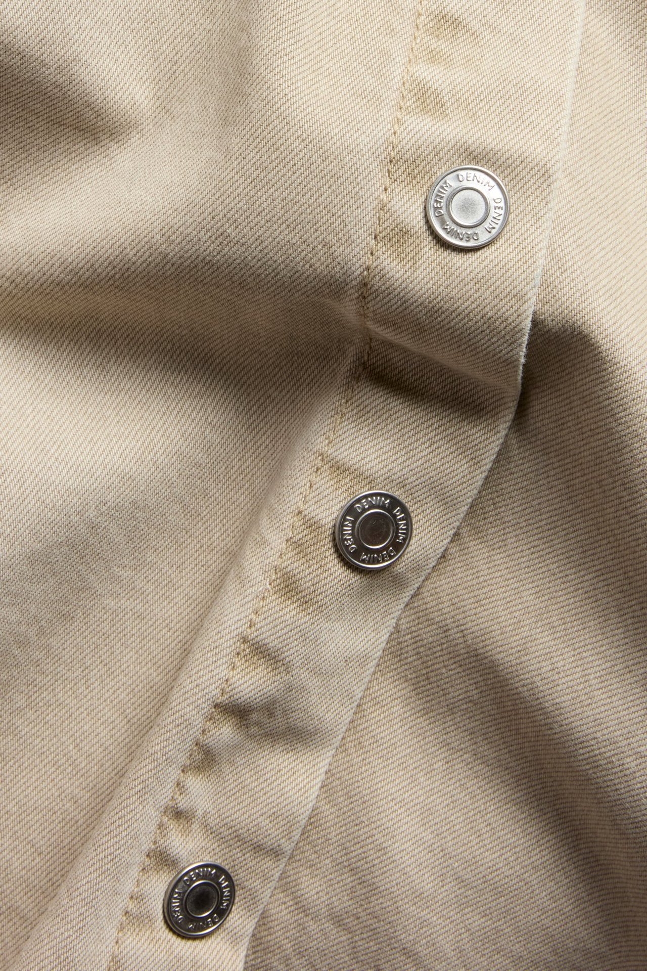 Zbliżenie beżowej koszuli twillowej z plisą i okrągłymi srebrnymi guzikami dżinsowymi.