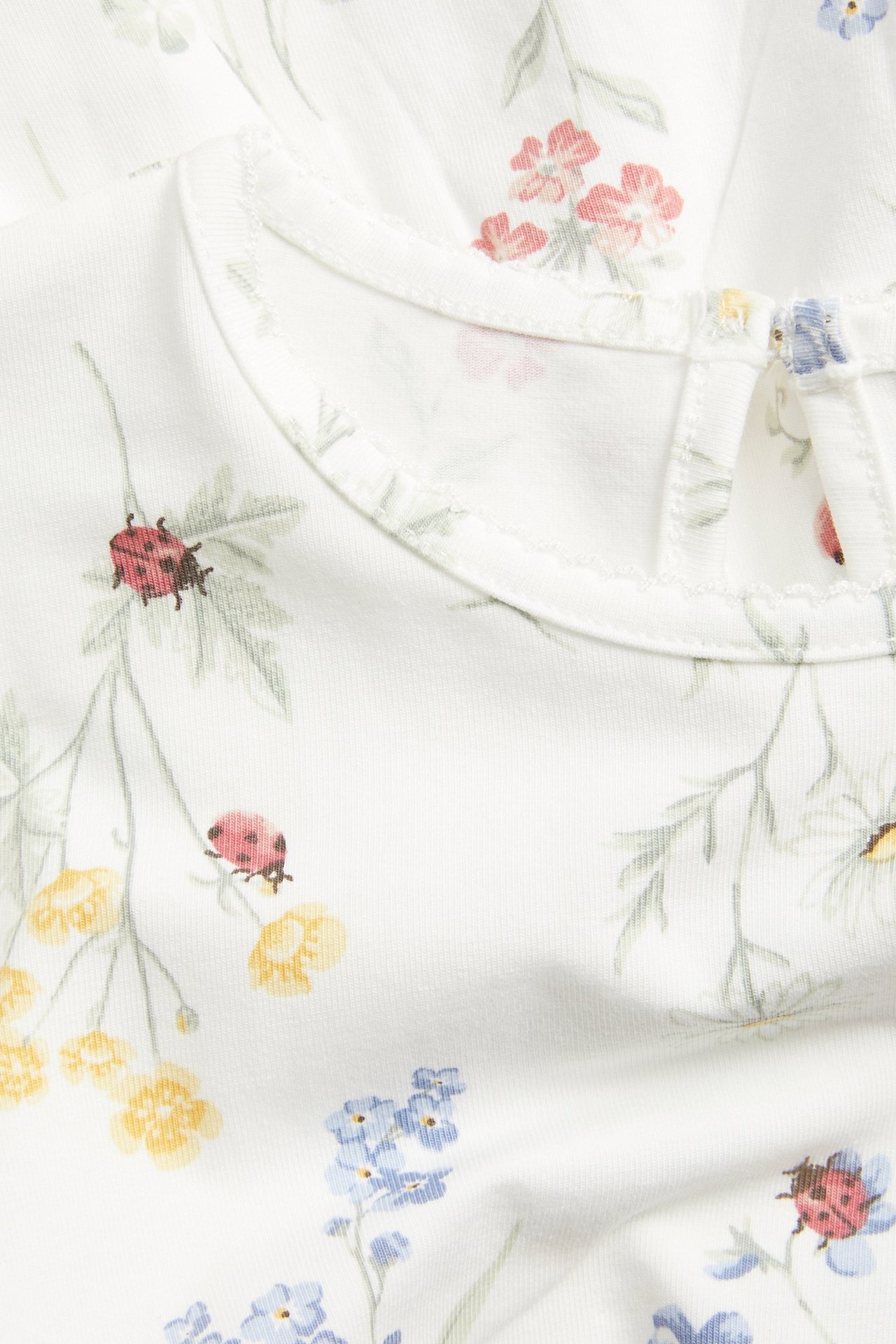 Närbild: offwhite blommig jerseypeplumtopp med nyckelpigor och nyckelhålsöppning med knapp.