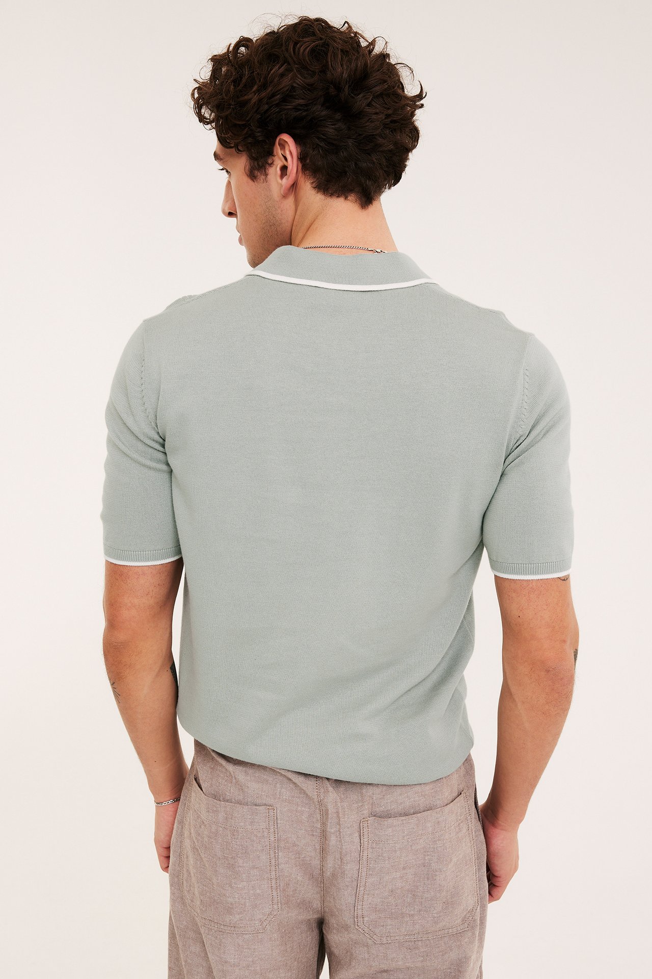 Ryggvy av en man i en ljusgrön stickad kortärmad pikétröja med vit kant och ljusbruna shorts.