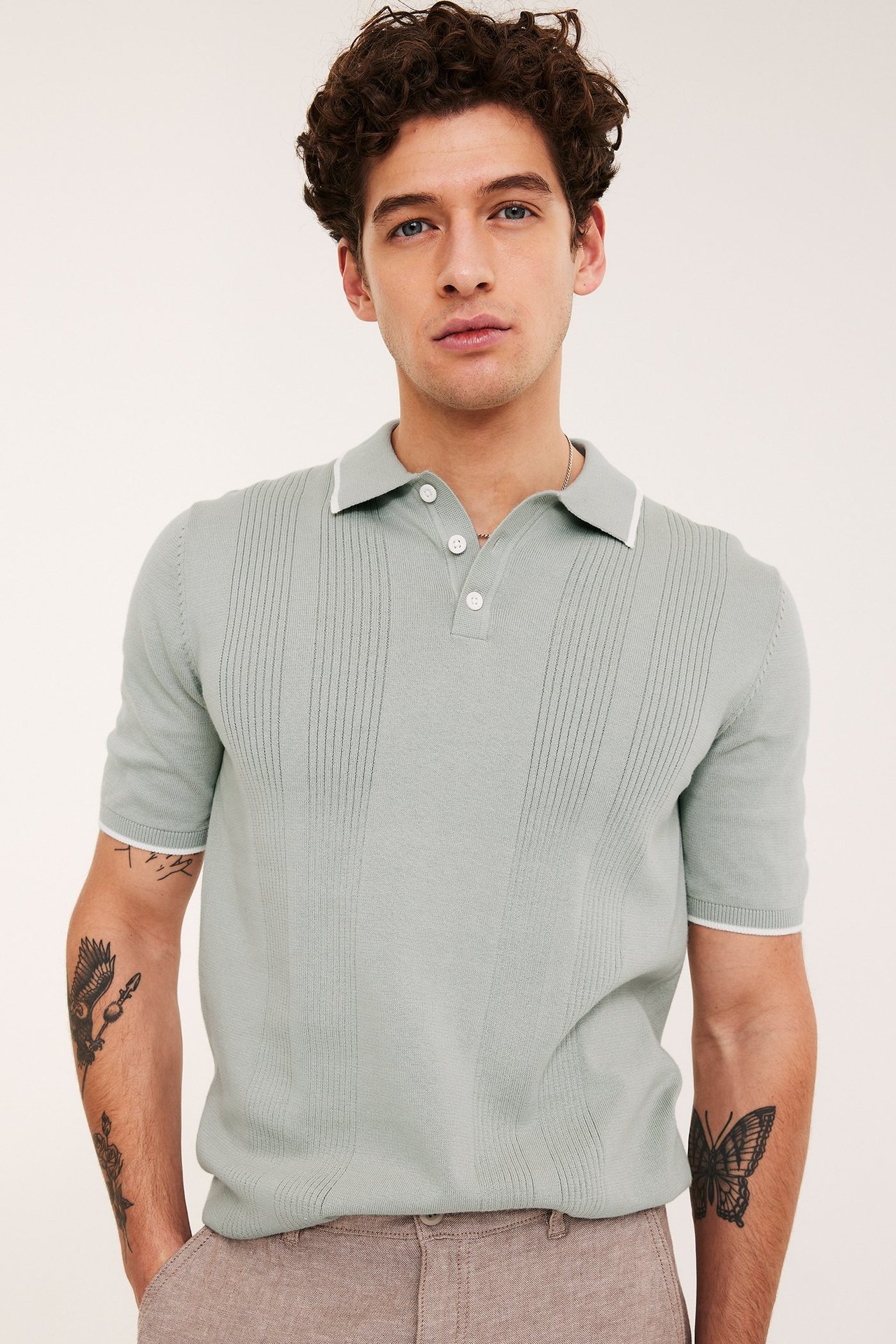 Front: Mann i lysegrønn strikket pologenser med hvitstripet krage og mansjetter. Lysebrune bukser.