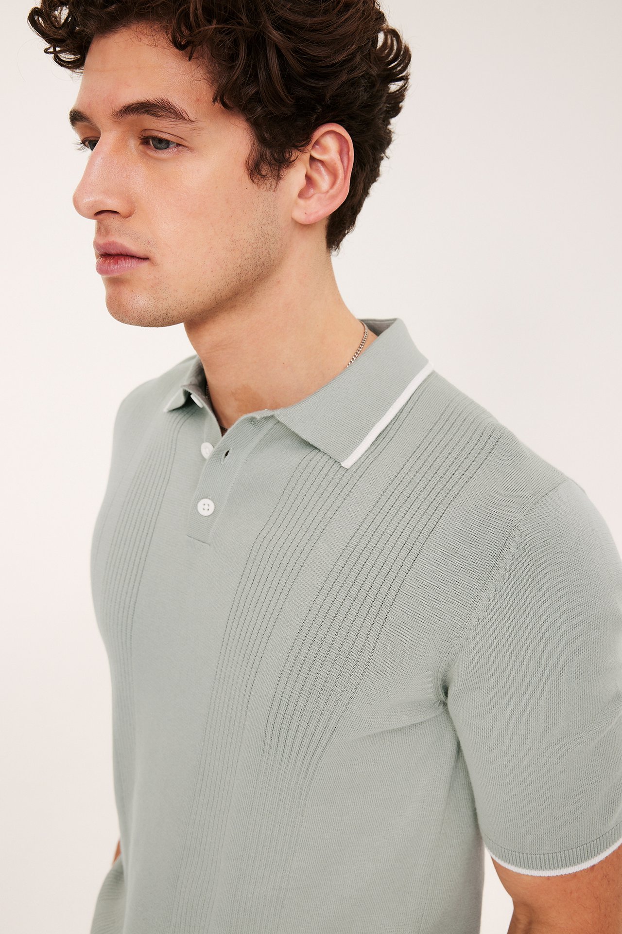 Sidovy, man i salviagrön stickad pikétröja med vitrandig krage, muddar och 3 knappar.