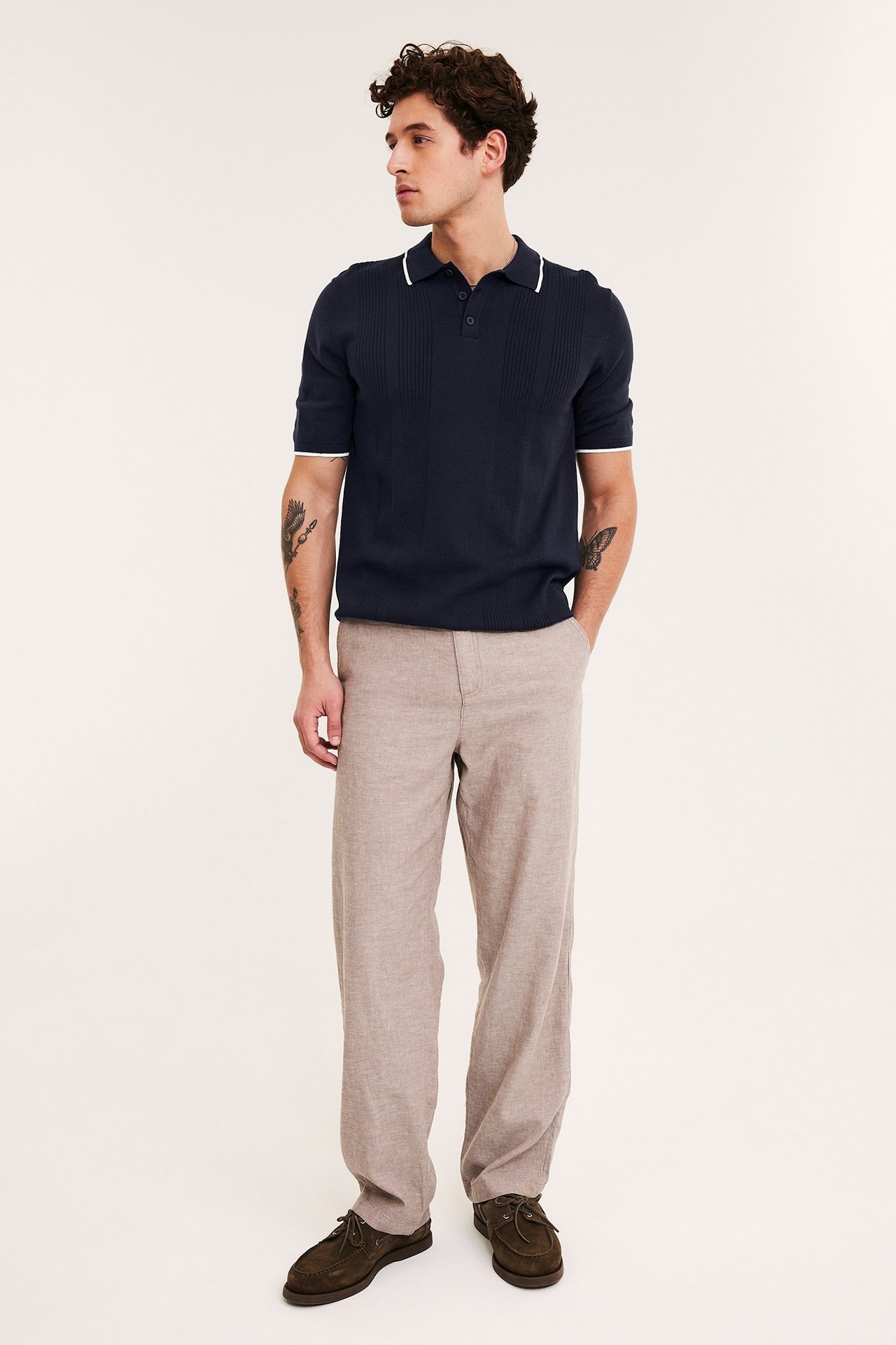 Frontbilde av en mann i mørkeblå strikket polo med hvit kant, beige bukse og brune båtsko.