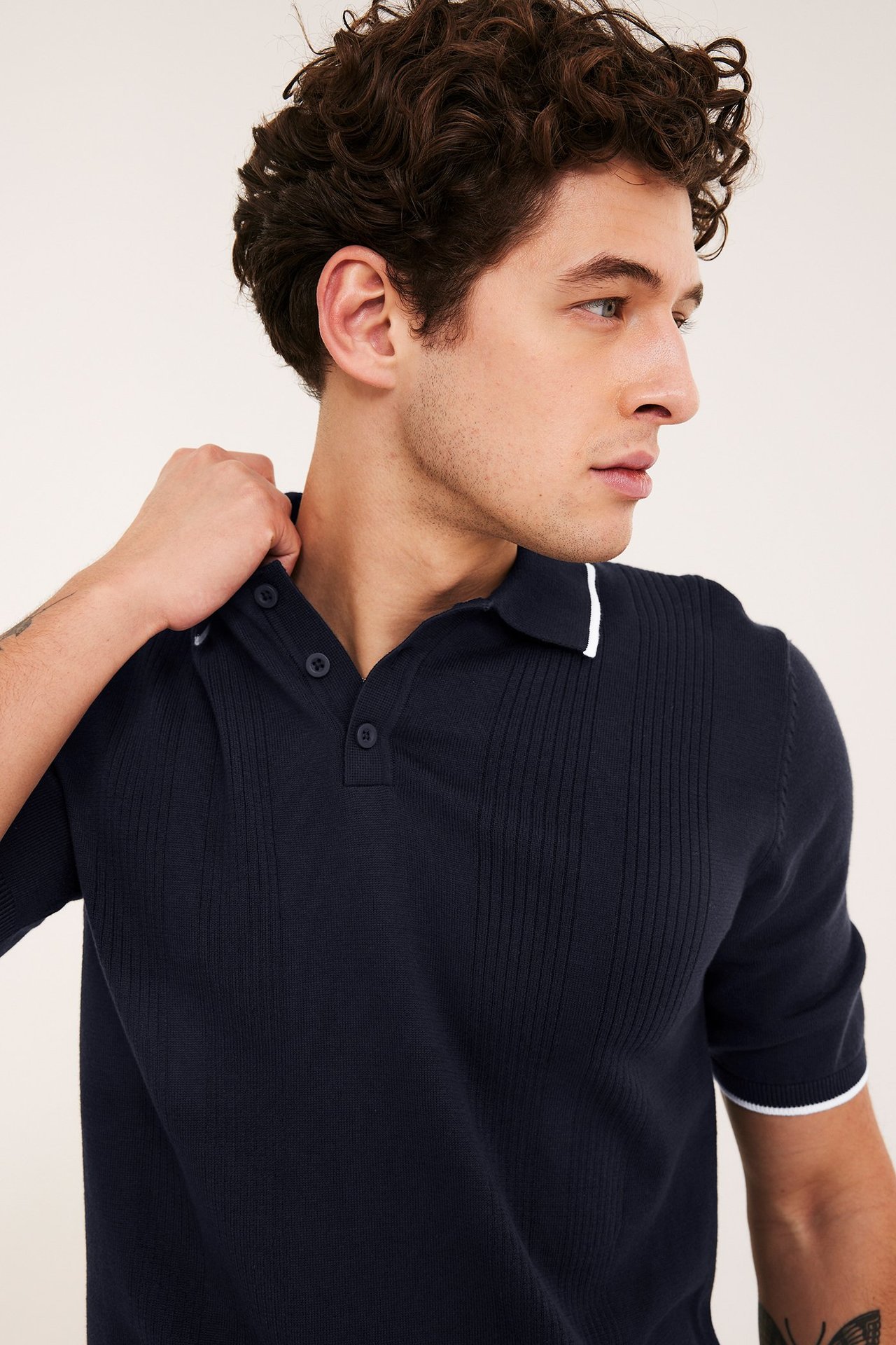 Zbliżenie mężczyzny w granatowej dzianinowej koszulce polo z 3 guzikami i białymi paskami na kołnierzu, rękawach.