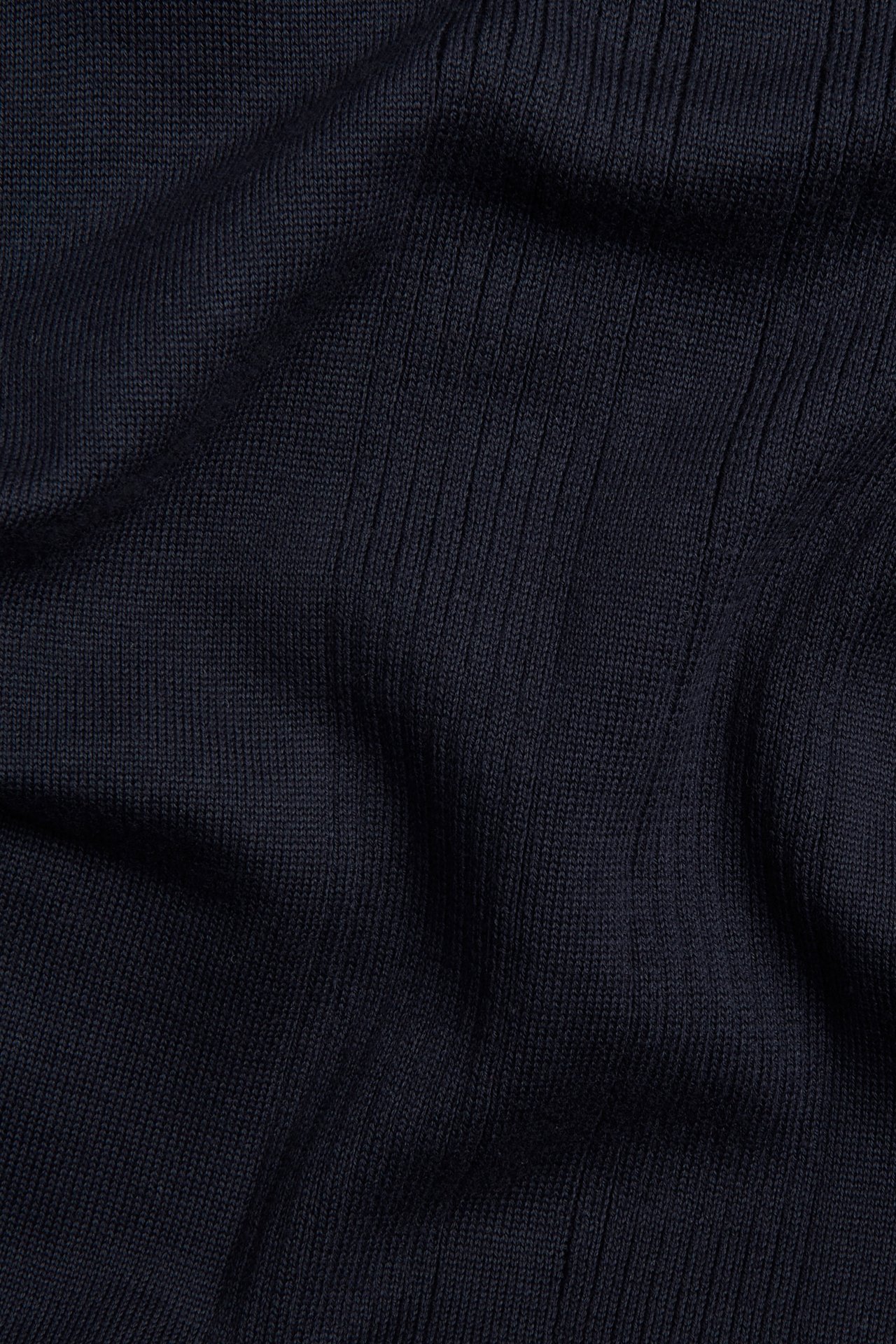 Lähikuva tummansinisestä, ribbineulotusta puuvillakankaasta pikeepaidasta.