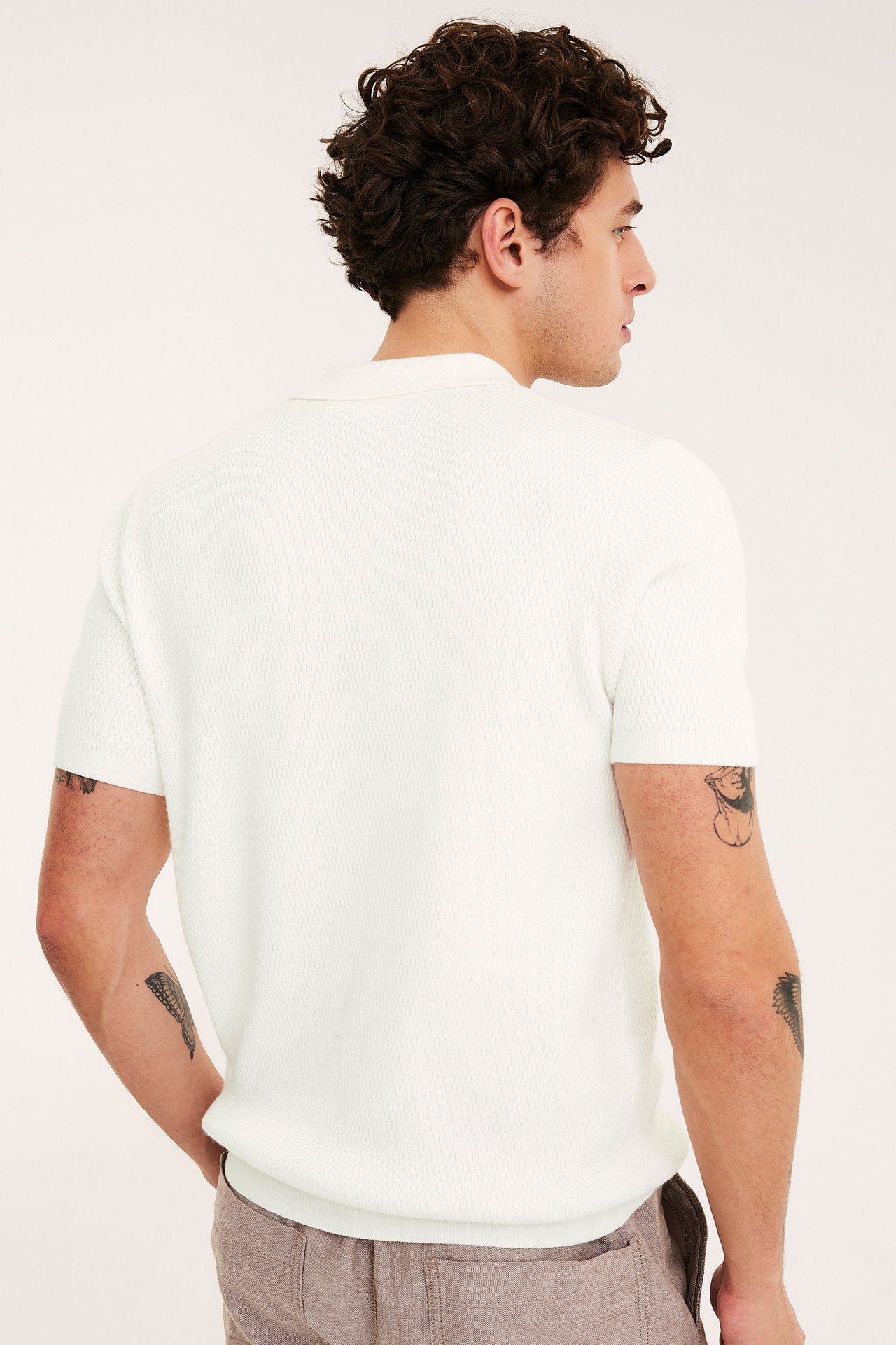 Bakside av mann i en offwhite, strukturstrikket kortermet piké og brune bukser.