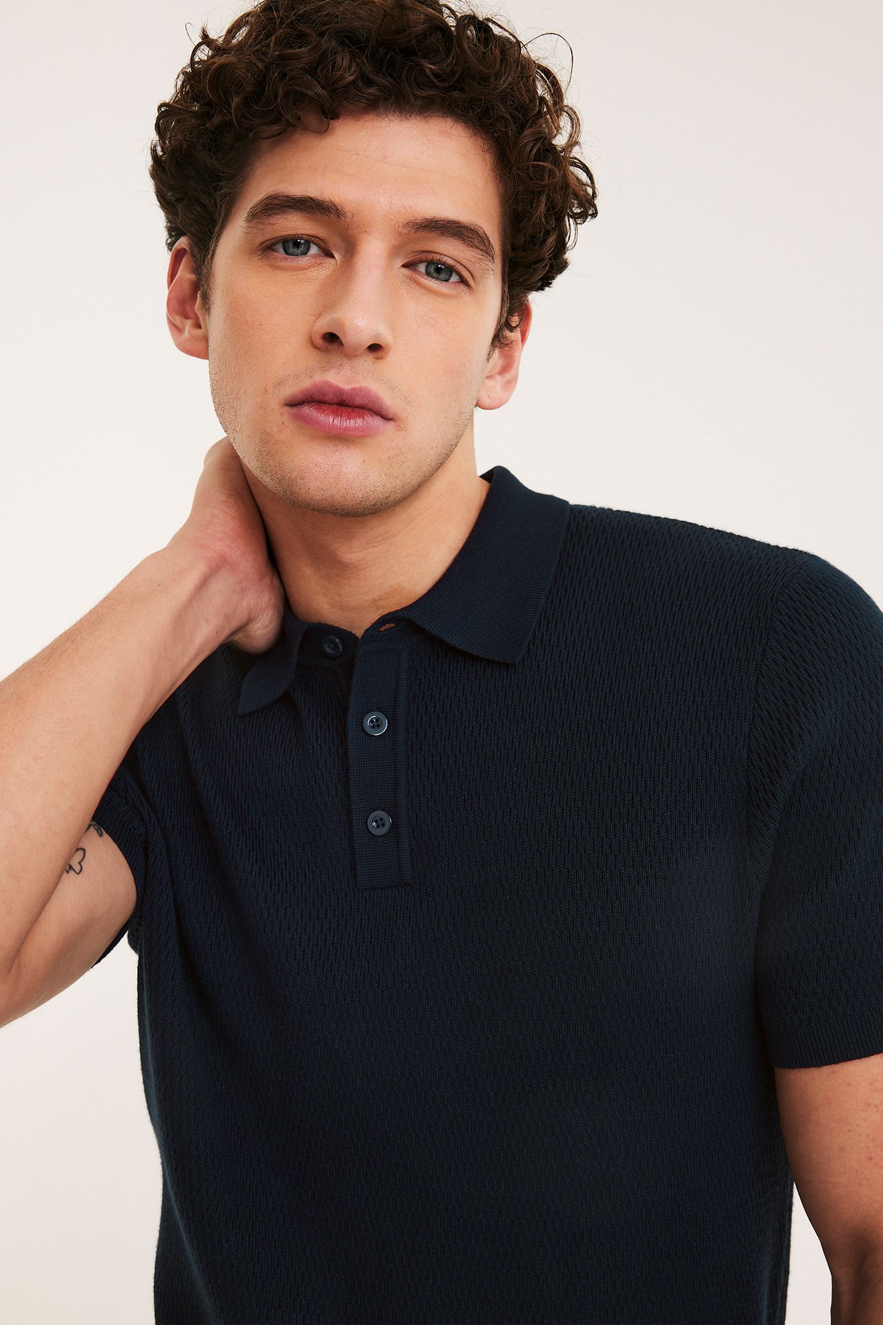 Nærbilde, forfra, av en mann i mørkeblå strukturstrikket kortermet poloskjorte med tre knapper.