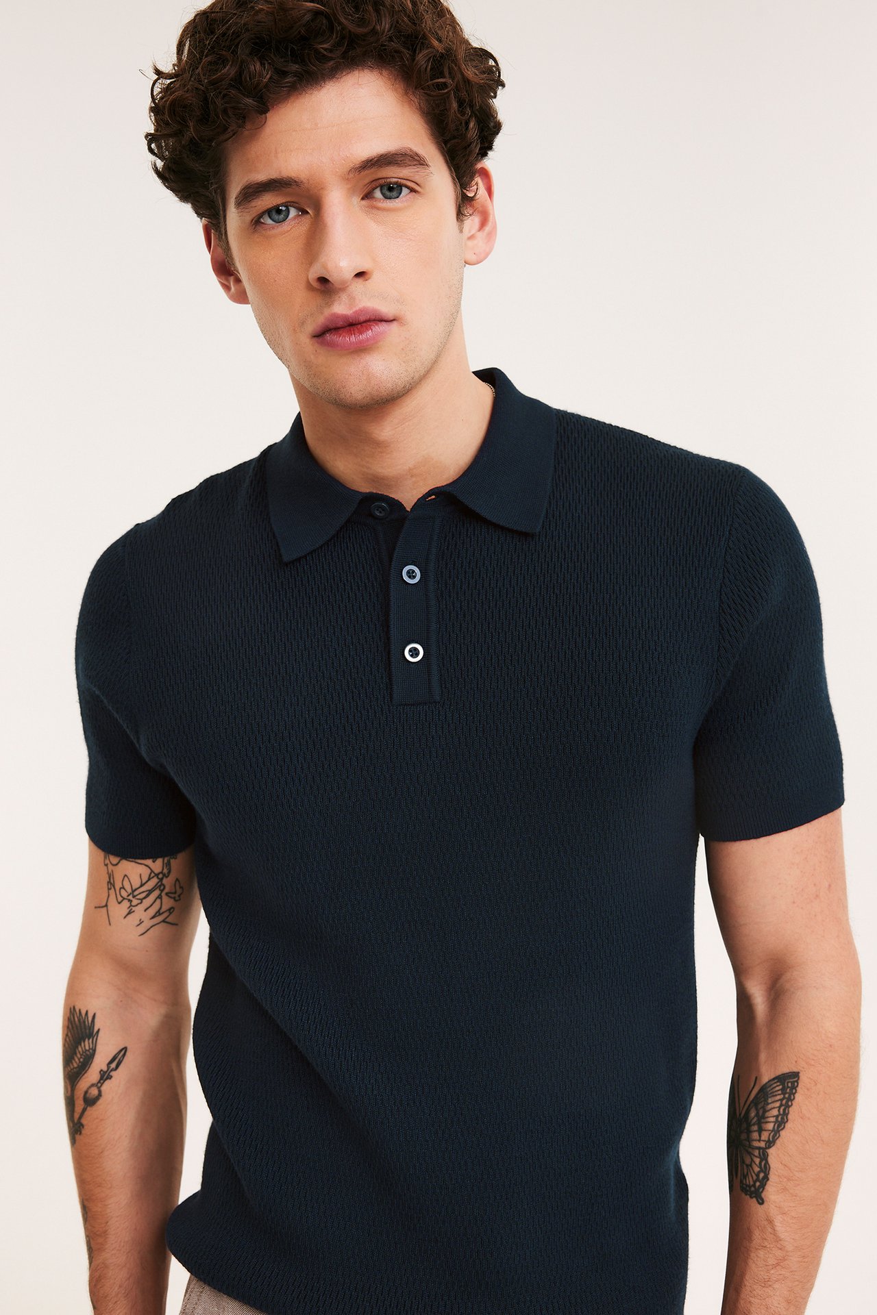 Edestä kuvattuna mies yllään tummansininen neulottu pikeepaita, jossa kolme nappia.