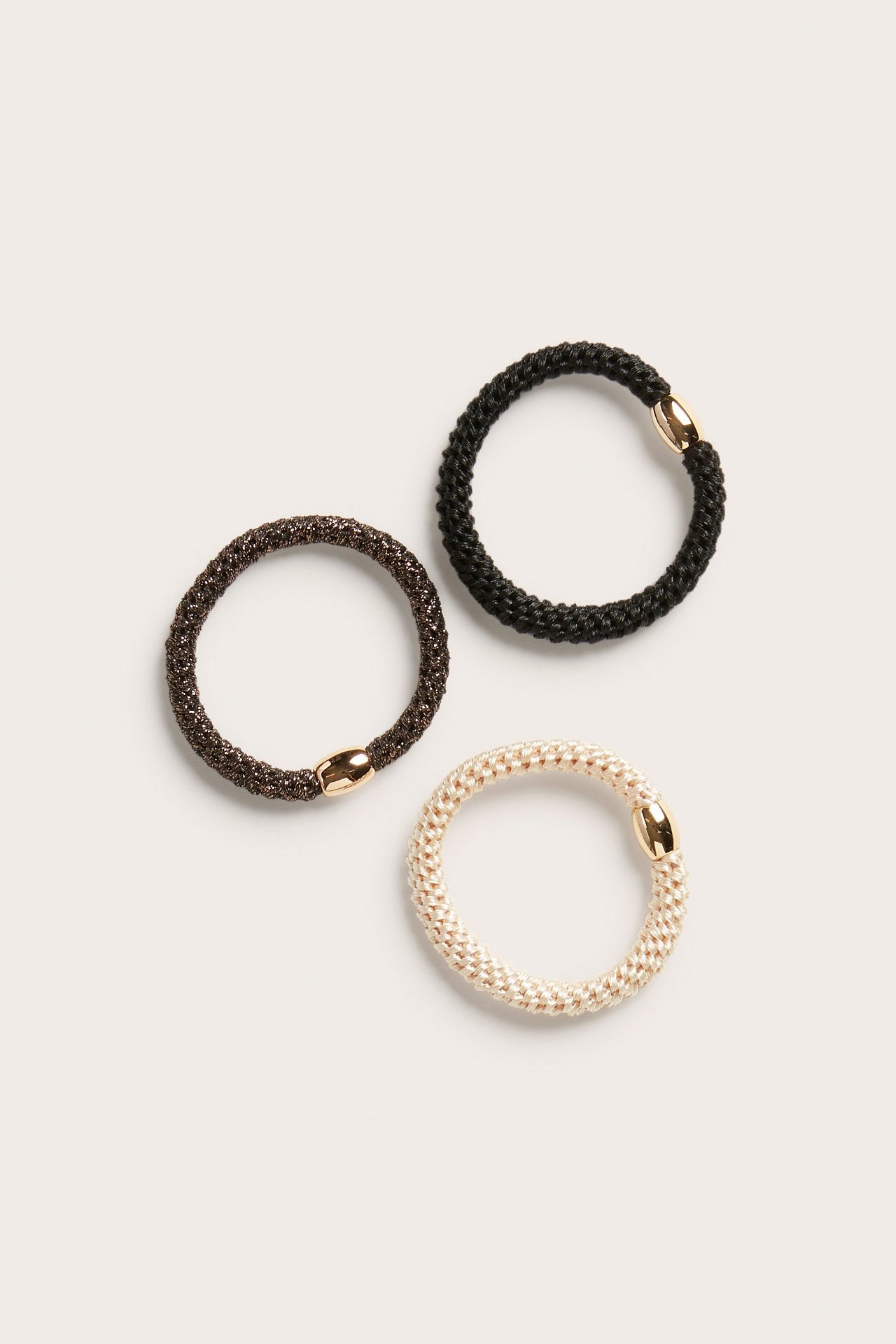 Ovanvy av tre tjocka flätade hårsnoddar i beige, brun och svart, med guldfärgade plastdetaljer.