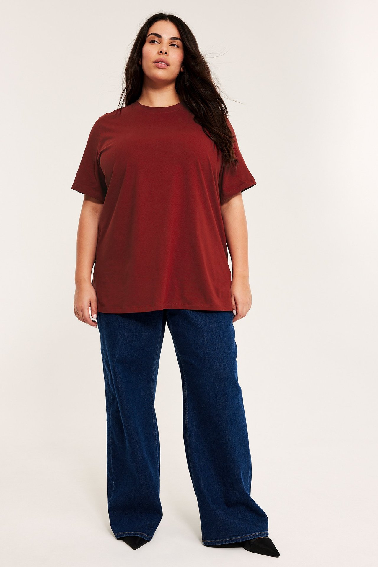 Framfra: kvinne i løs rød bomulls-lang t-skjorte, mørkeblå vide jeans, svarte spisse sko.