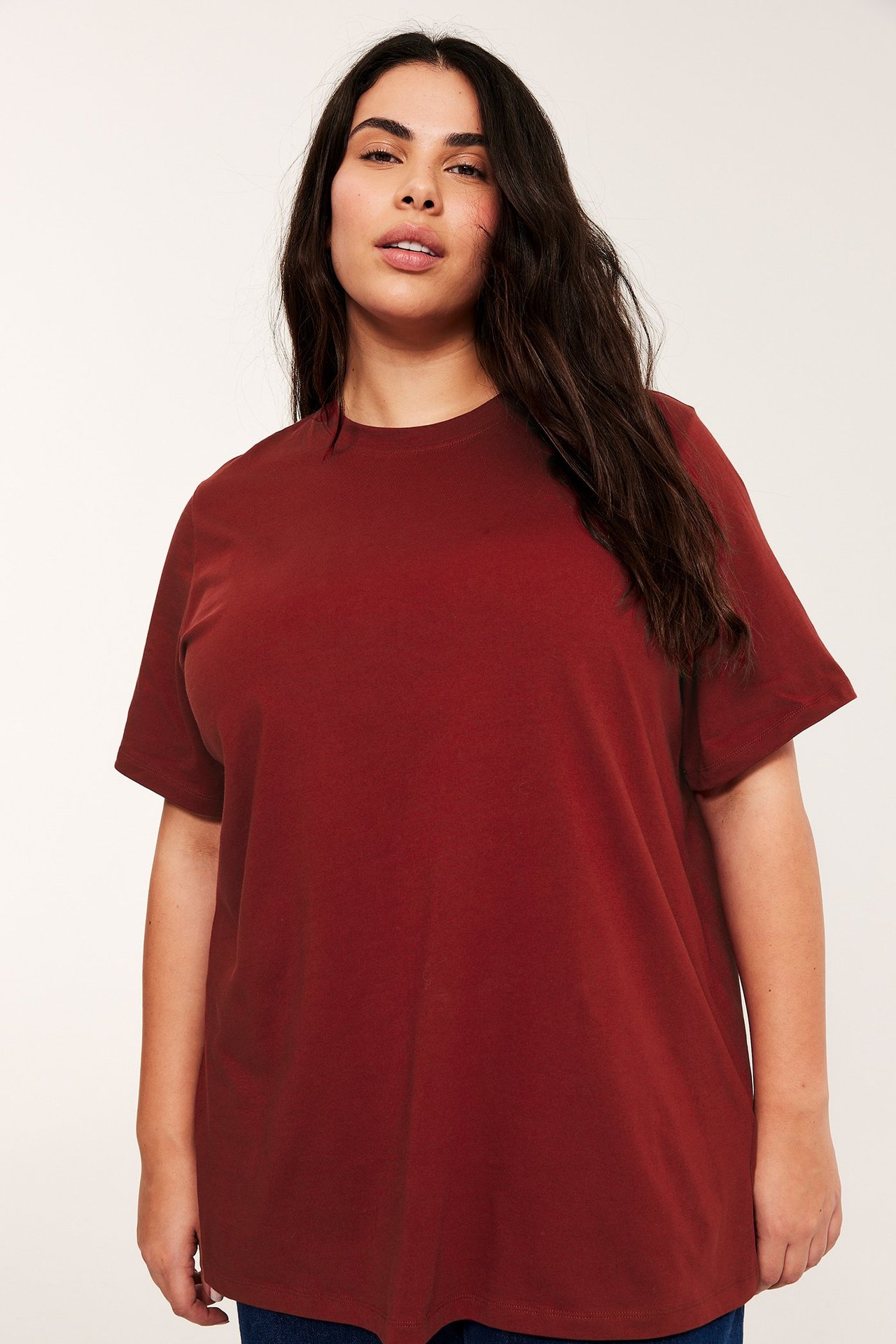 Forfra: en kvinne i en løstsittende, ensfarget rød, lang bomullst-skjorte med rund hals.