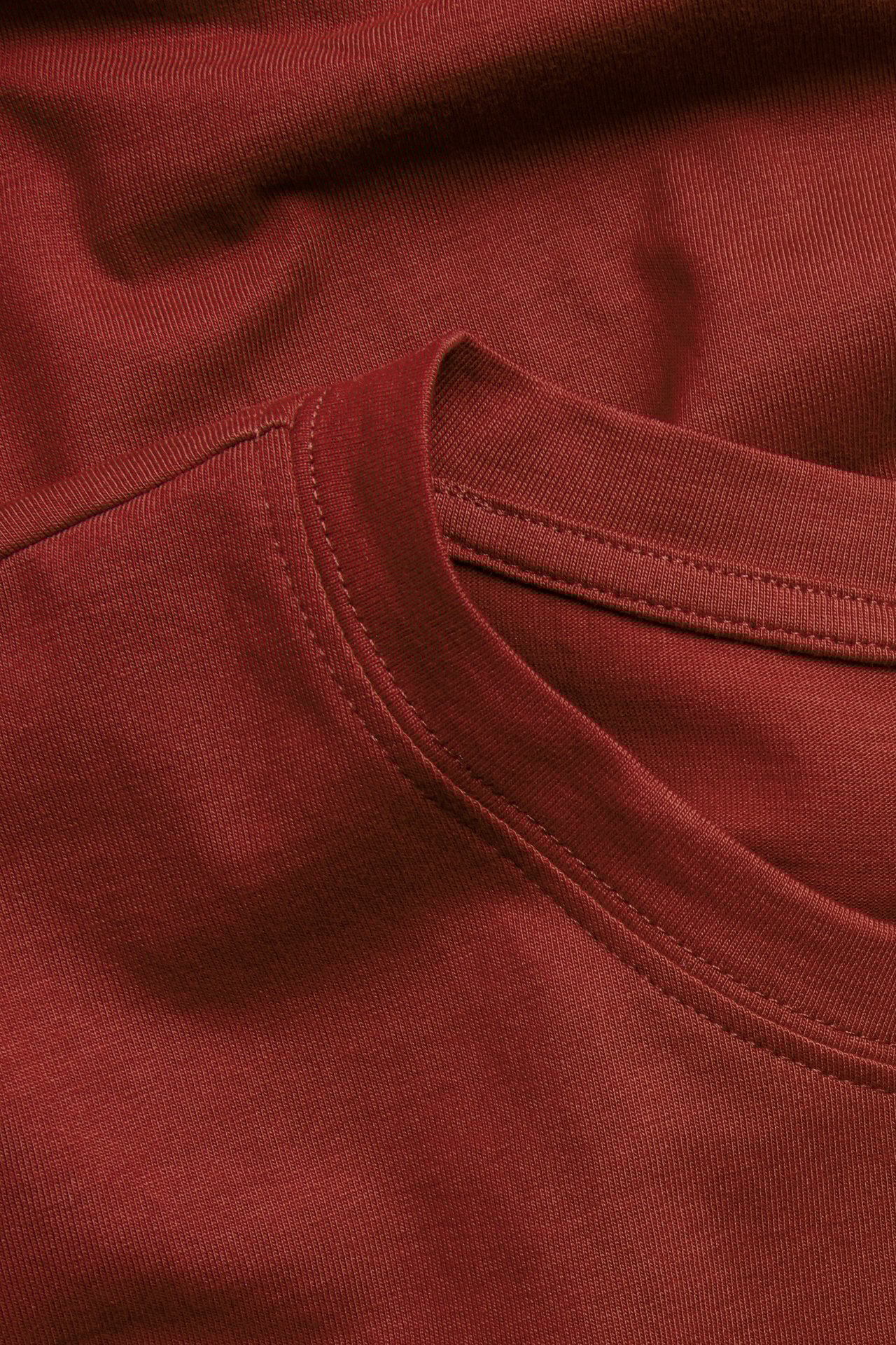 Lähikuva yksivärisestä punaisesta pitkästä puuvilla-T-paidasta, jossa on pyöreä pääntie.