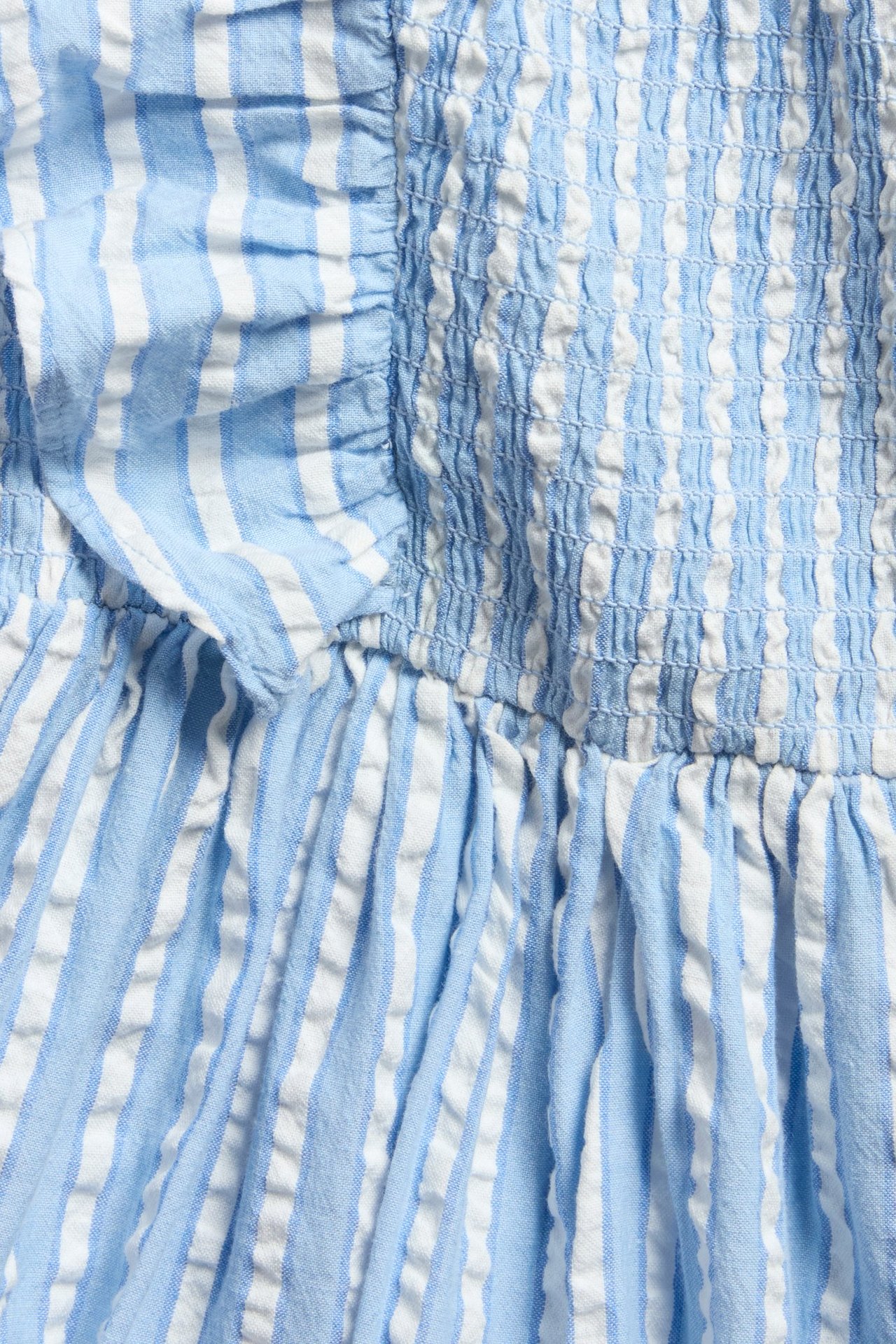 Nærbilde av lys blå og hvitstripet bomulls-seersucker-kjole med smock og volang.