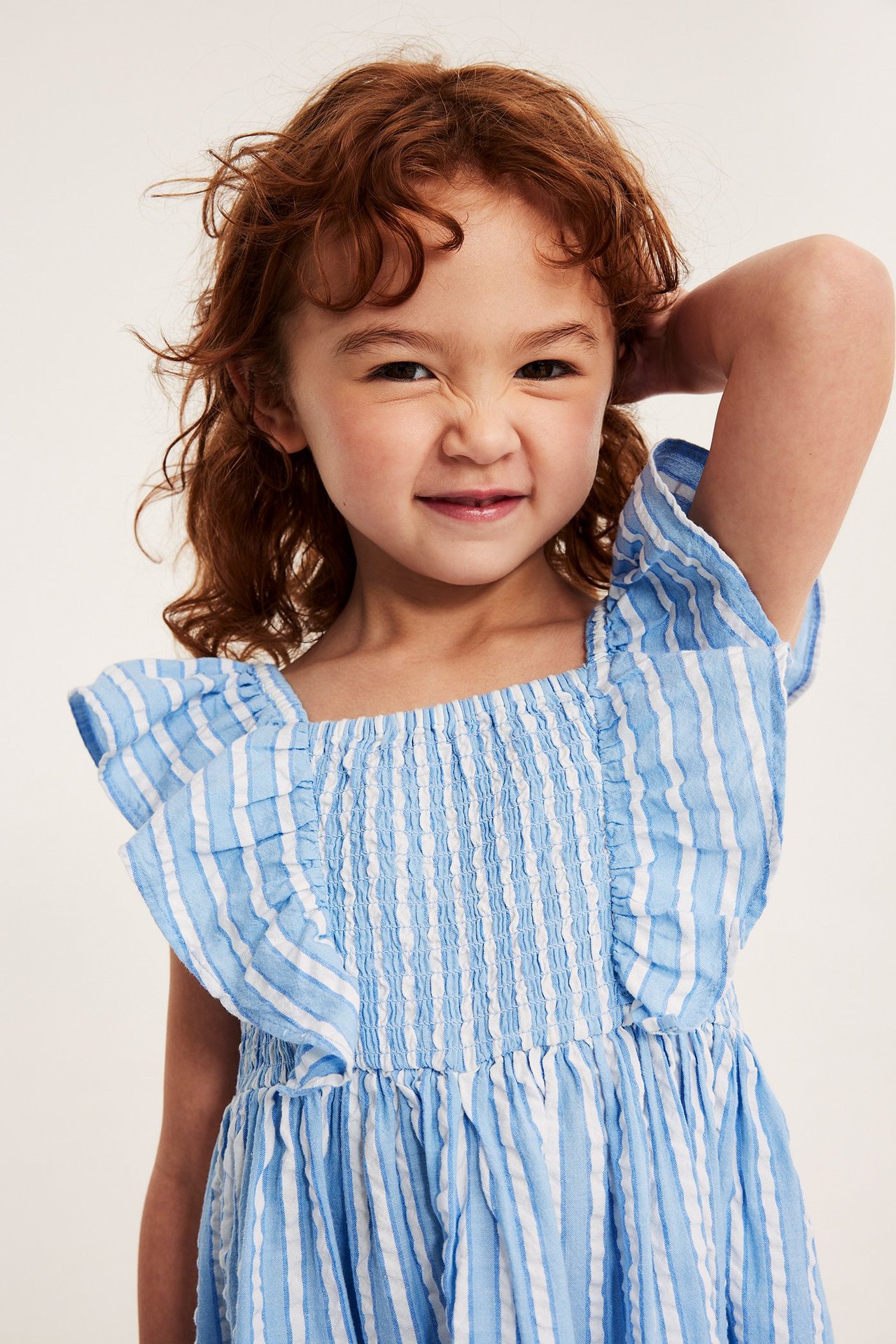 Edestä päin, lapsi vaaleansinivalkoraidallisessa puuvillabäckebölja-mekossa, jossa smock-yläosa ja röyhelöt.