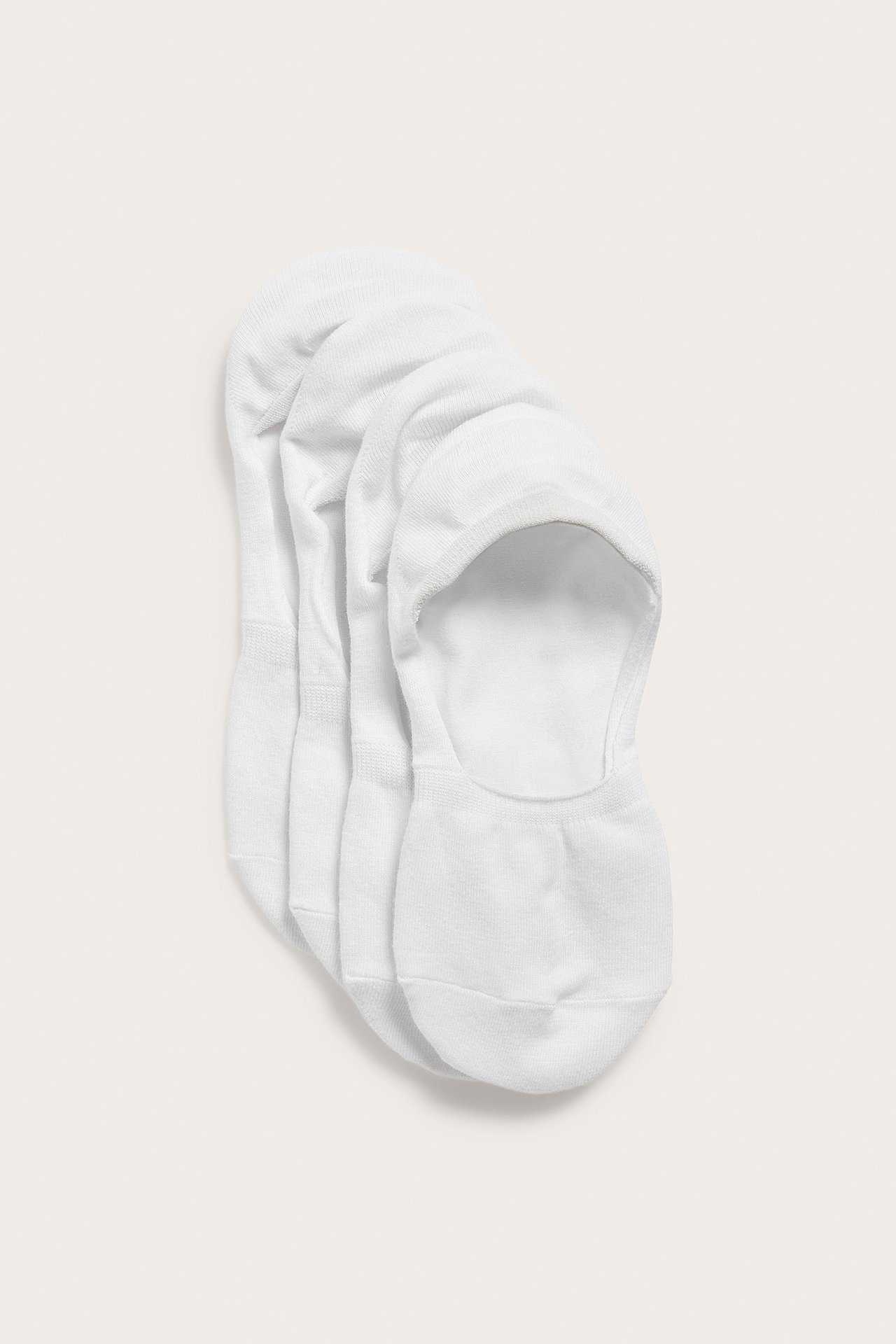 Widok z góry czterech białych, jednolitych, niewidocznych skarpetek z mieszanki bawełny.