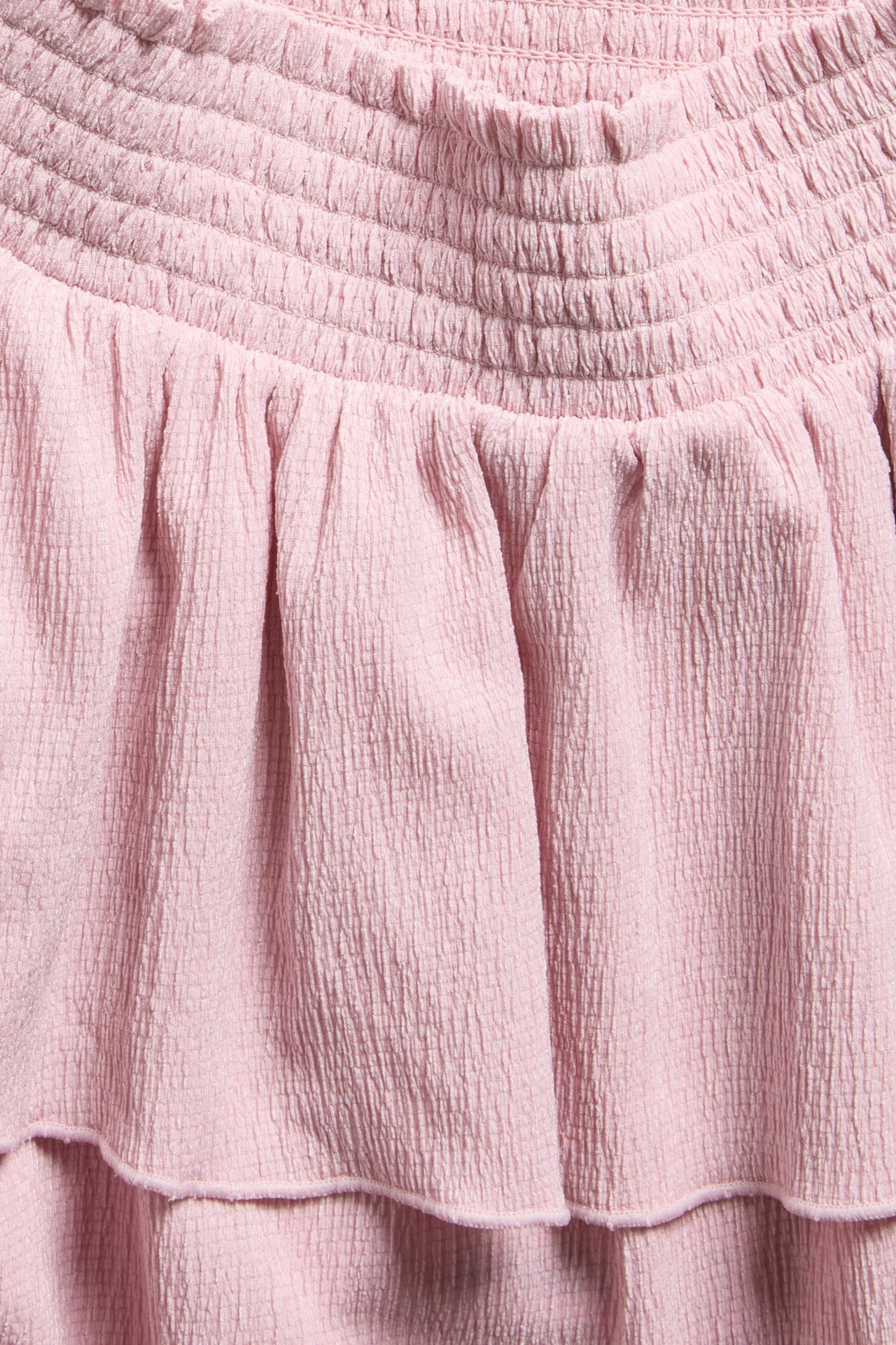 Zbliżenie na jasnoróżową, kreszowaną spódnicę z falbanami i marszczonym pasem.