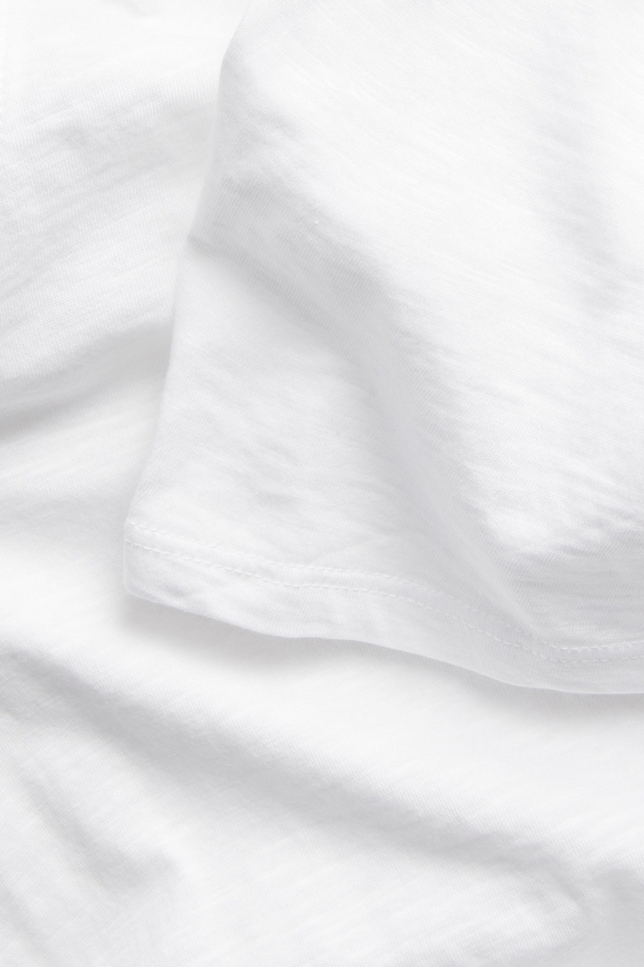 Lähikuva valkoisesta puuvillaisesta t-paidan kankaasta, joka näyttää sen teksturoidun pinnan ja ommellun helman.