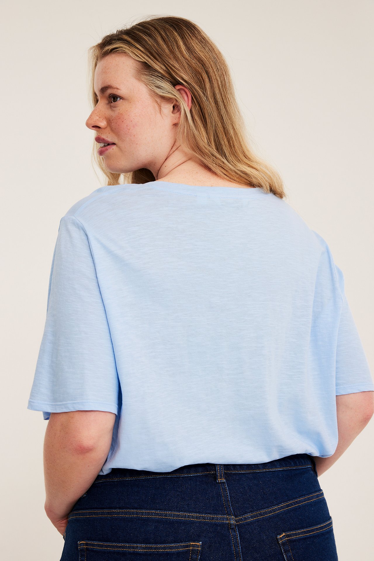 Naisen sivukuva, yllään vaaleansininen lyhythihainen puuvillapaita ja tummansiniset farkut.