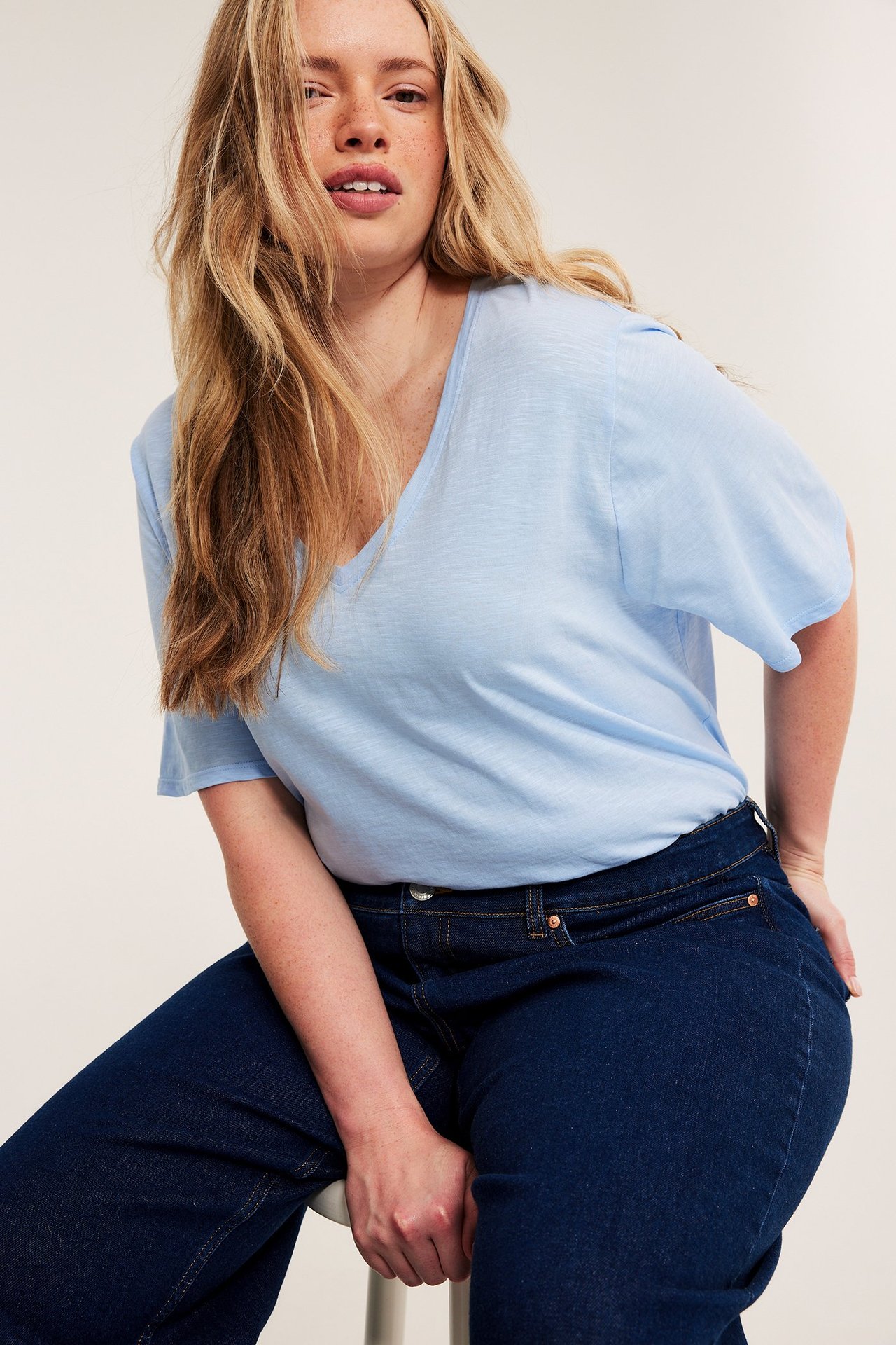 Edestäpäin: nainen vaaleansinisessä V-aukkoisessa puuvillapuserossa ja tummansinisissä farkuissa.