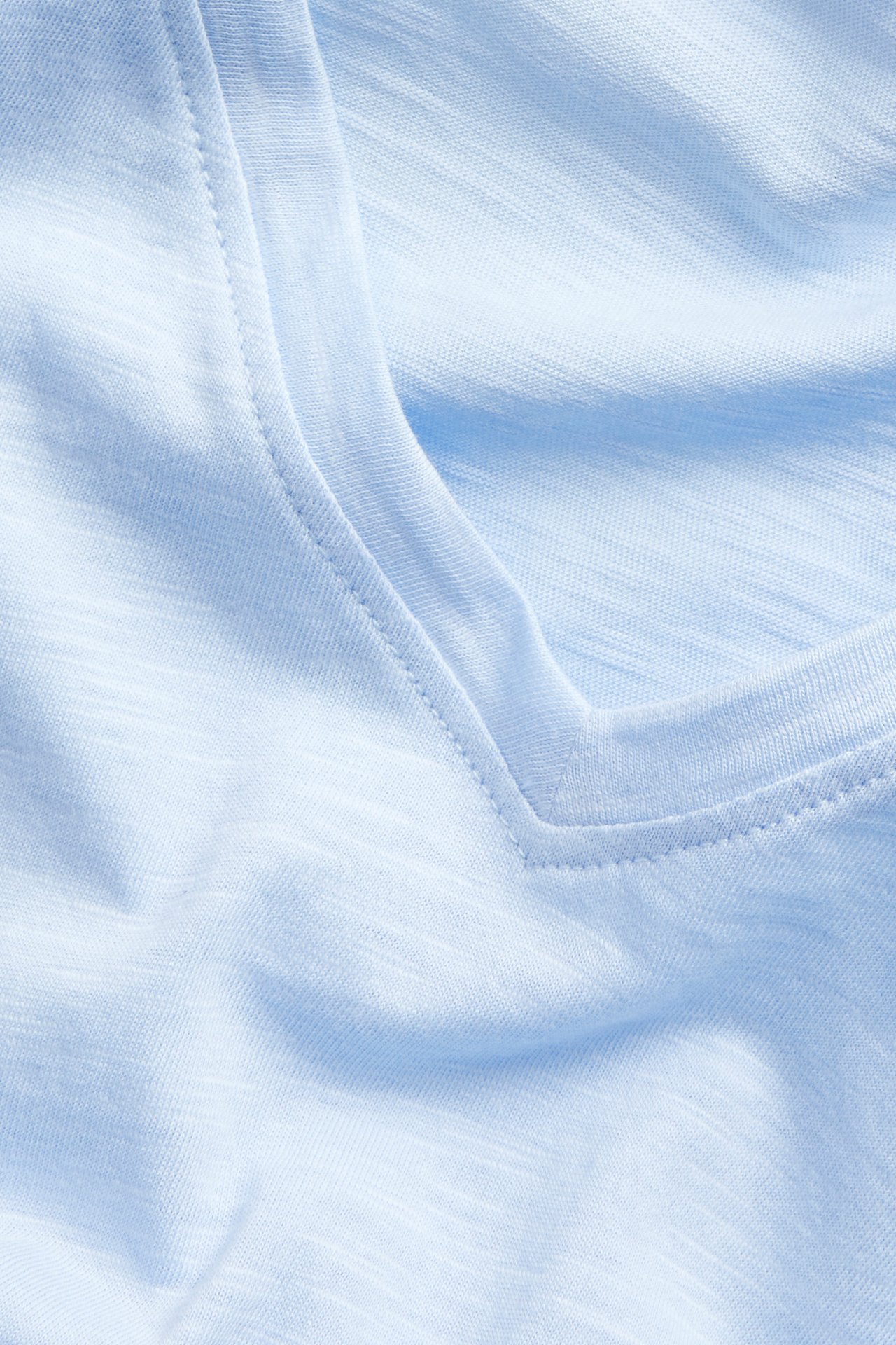 Nærbilde av en lyseblå V-hals bomulls-t-skjorte med synlig stofftekstur.