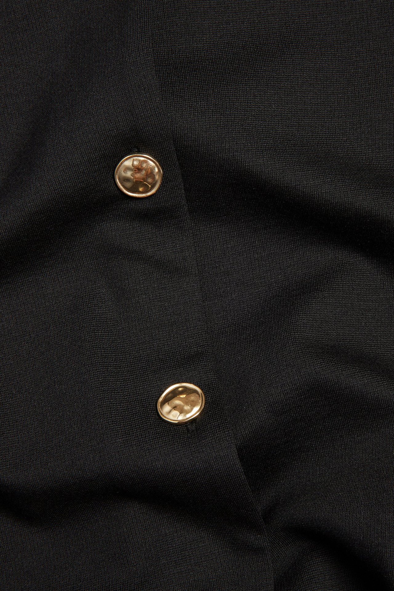 Zbliżenie czarnej marynarki damskiej z dzianiny Punto z dwoma okrągłymi, teksturowanymi złotymi guzikami.
