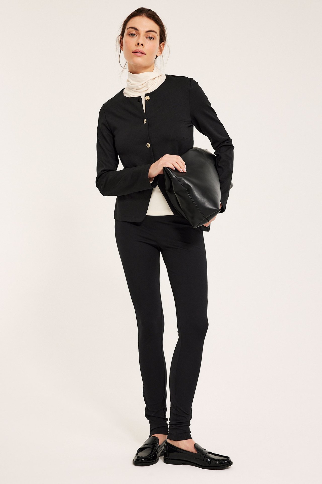 Widok z przodu: Kobieta w czarnym żakiecie Punto z dzianiny z guzikami, białym topie, czarnych spodniach i czarnej torbie.