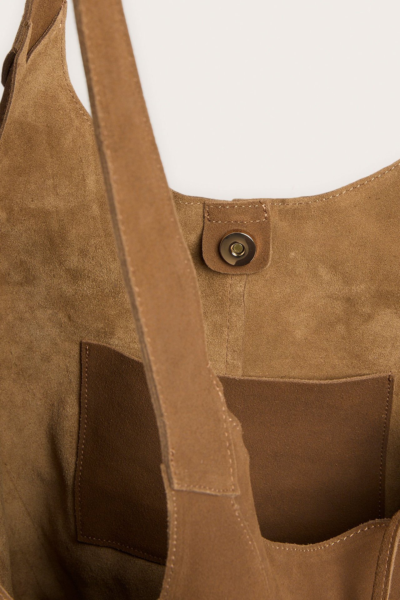 Nærbilde av en lysebrun semsket toteveske med magnetisk lukking og en innerlomme i skinn.