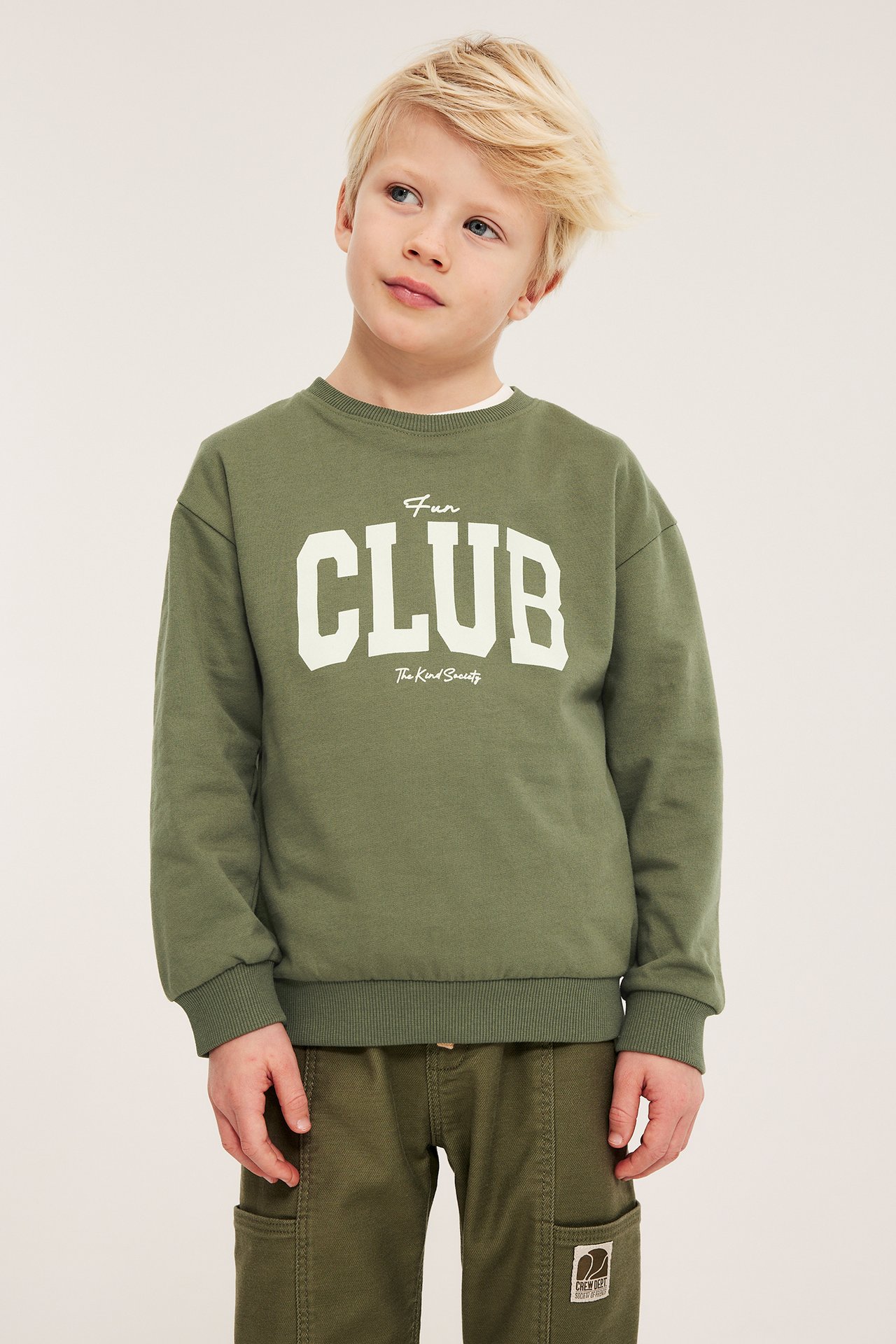 Dziecko w ciemnozielonej bluzie z nadrukiem „Fun CLUB” i ciemnozielonych spodniach cargo.