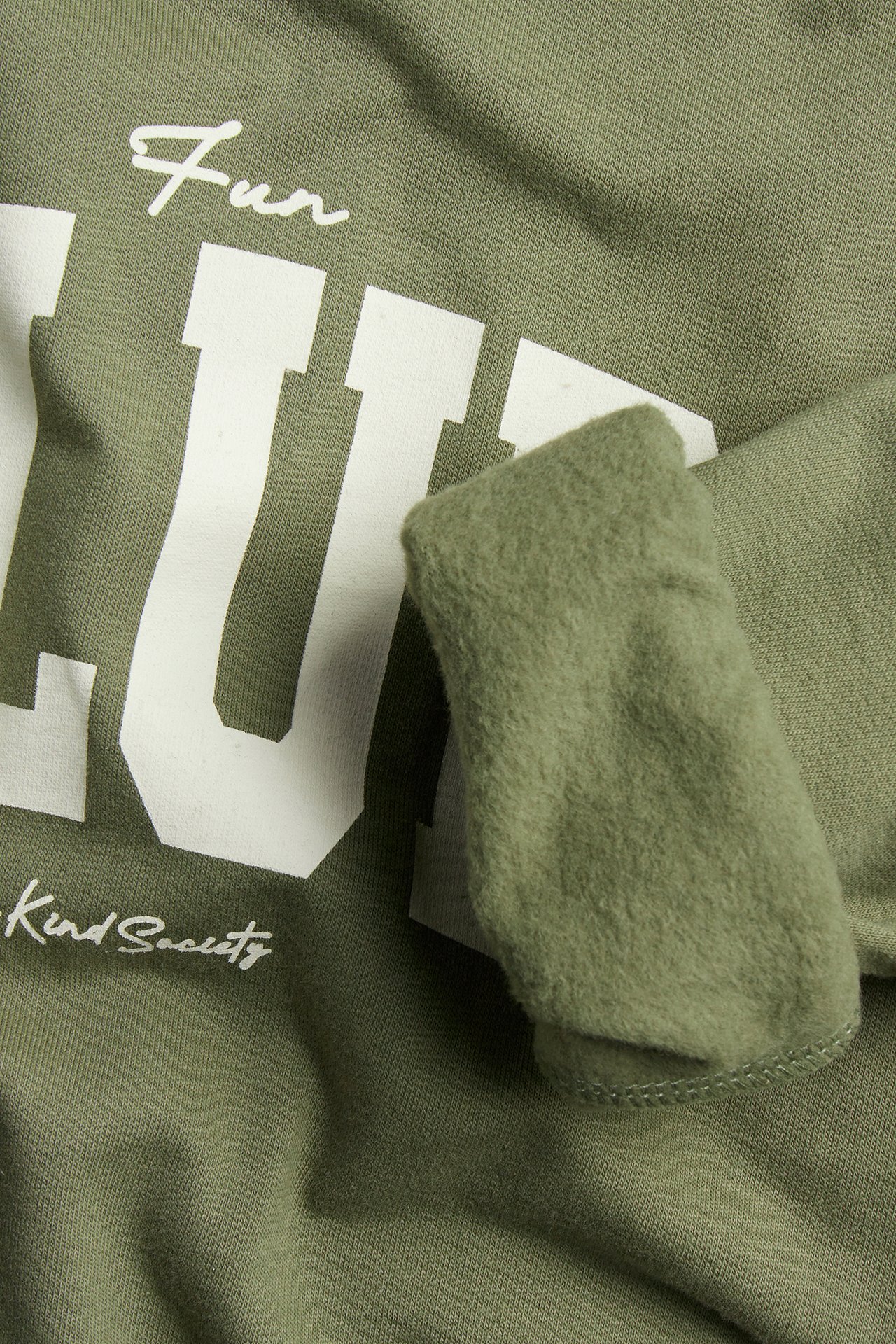 Närbild på en mörkgrön sweatshirt i bomull med vitt texttryck framtill och ribbad mudd.