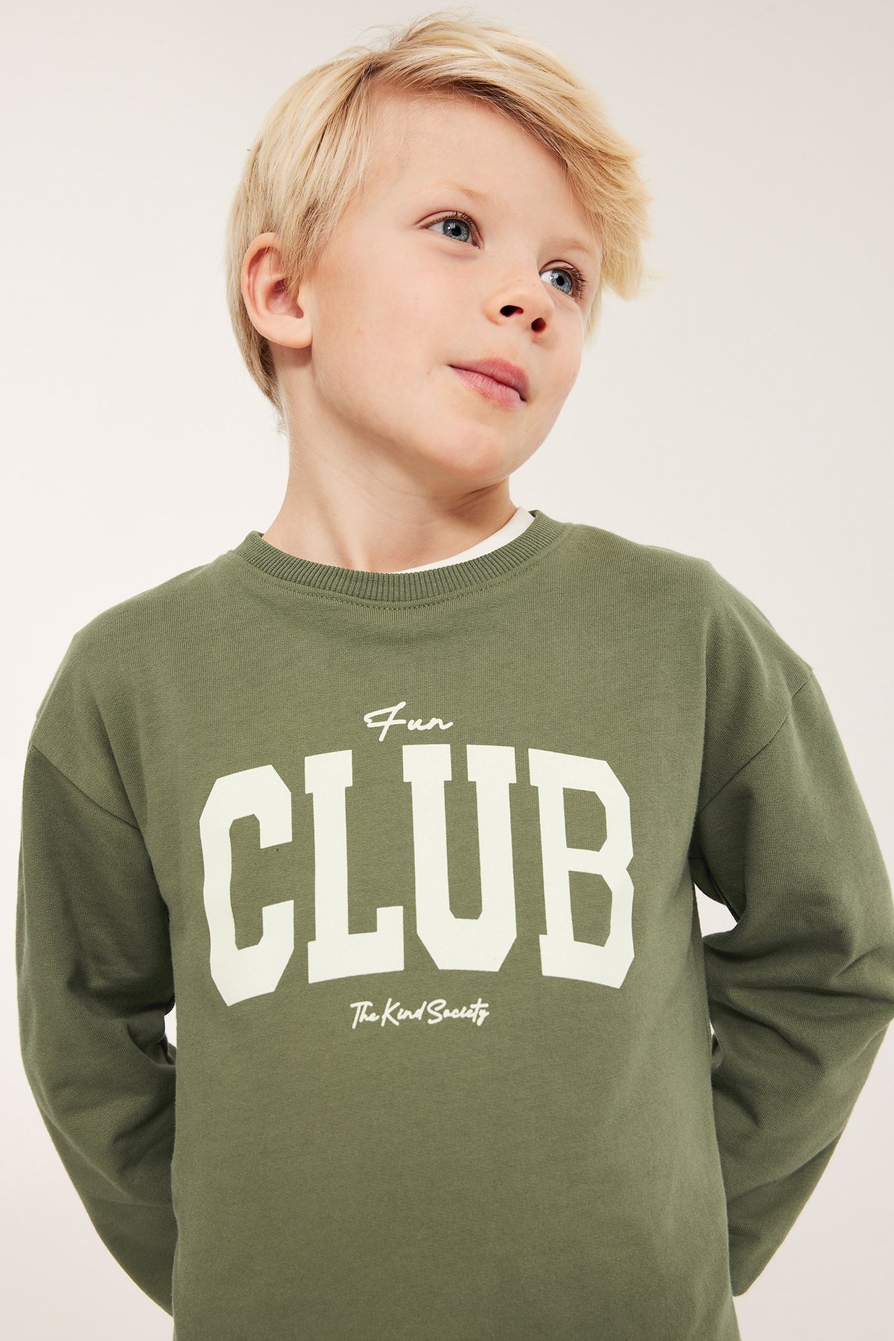 Forfra, et barn i en mørkegrønn bomullssweatshirt med hvitt "FUN CLUB" teksttrykk foran.