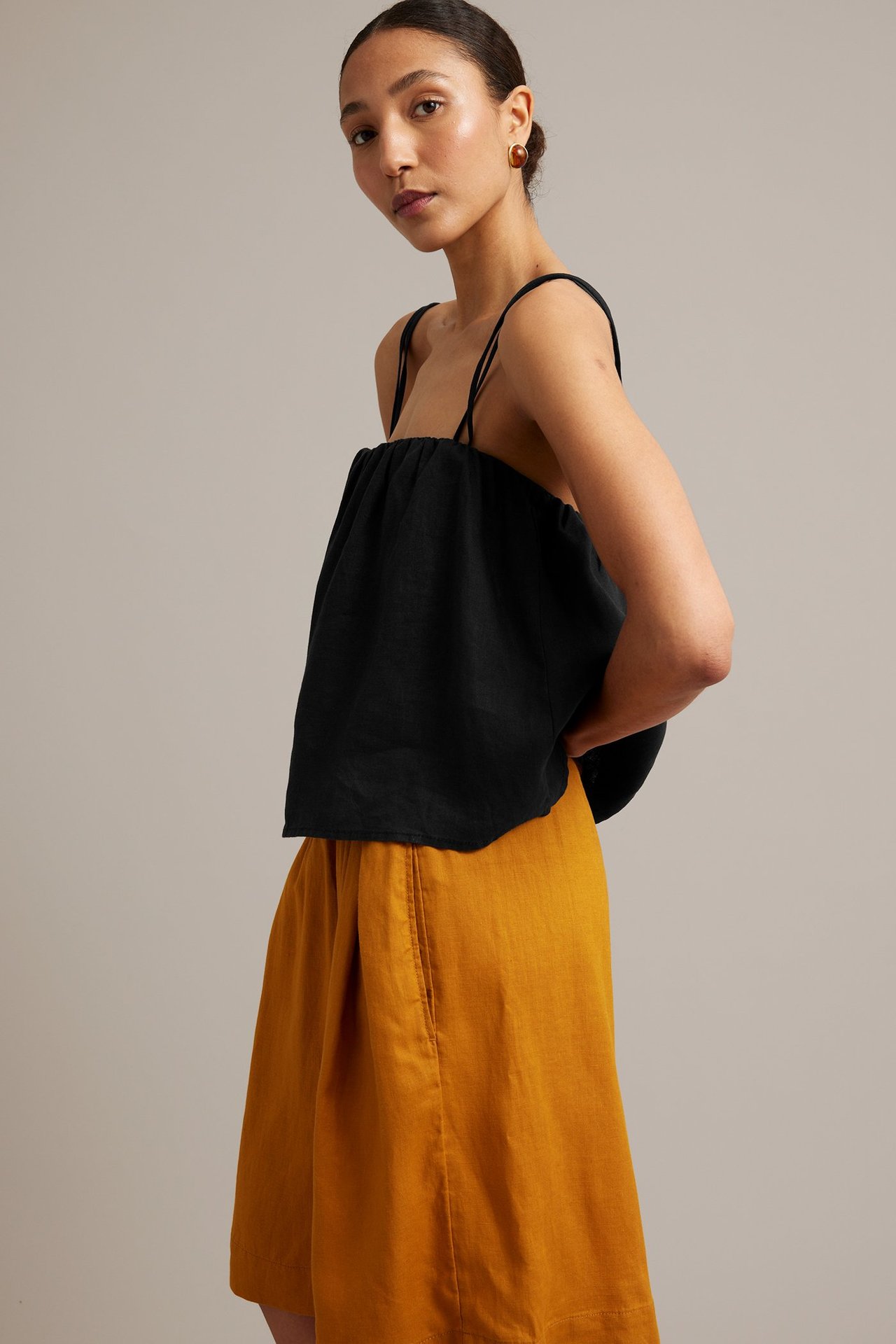 Framifrån: Kvinna i svart linne, senapsgula vida shorts och bärnstensfärgade örhängen.