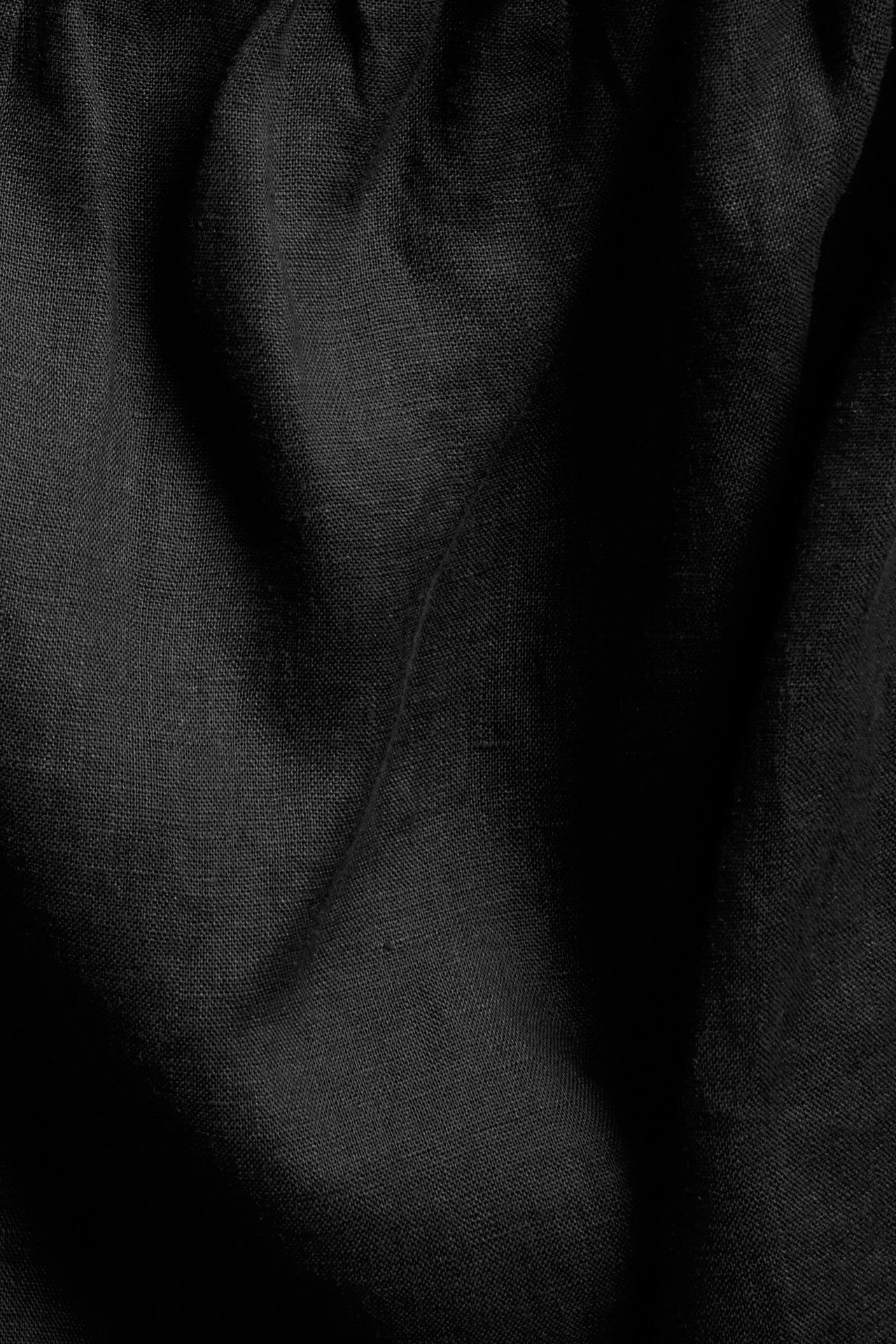 Närbild av svart enfärgad linfabrik med diskret textur och mjuka veck.