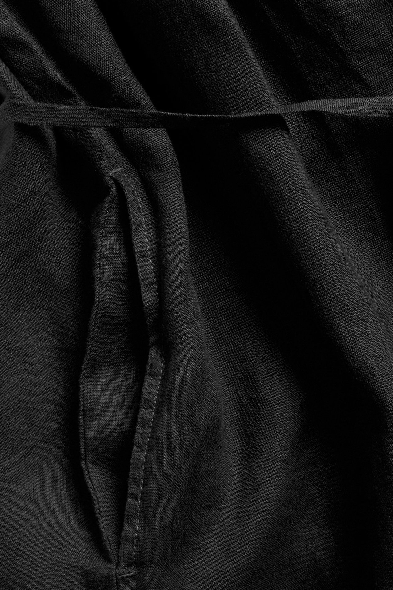 Närbild på en svart linneklänning med knytskärp, visar en sidoficka.