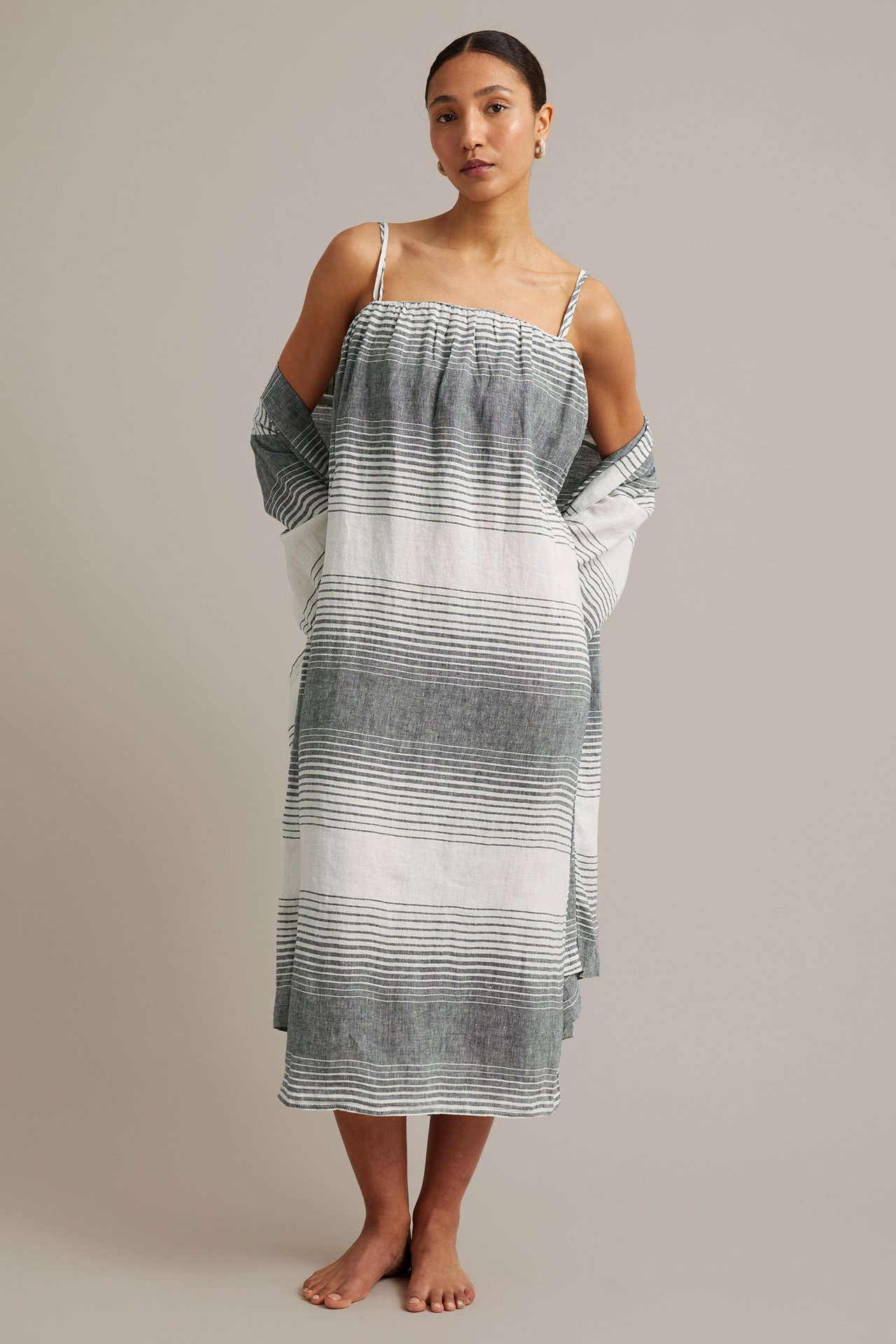 En kvinna framifrån i randig mörkblå och vit linneklänning med spagettiband och matchande sjal.