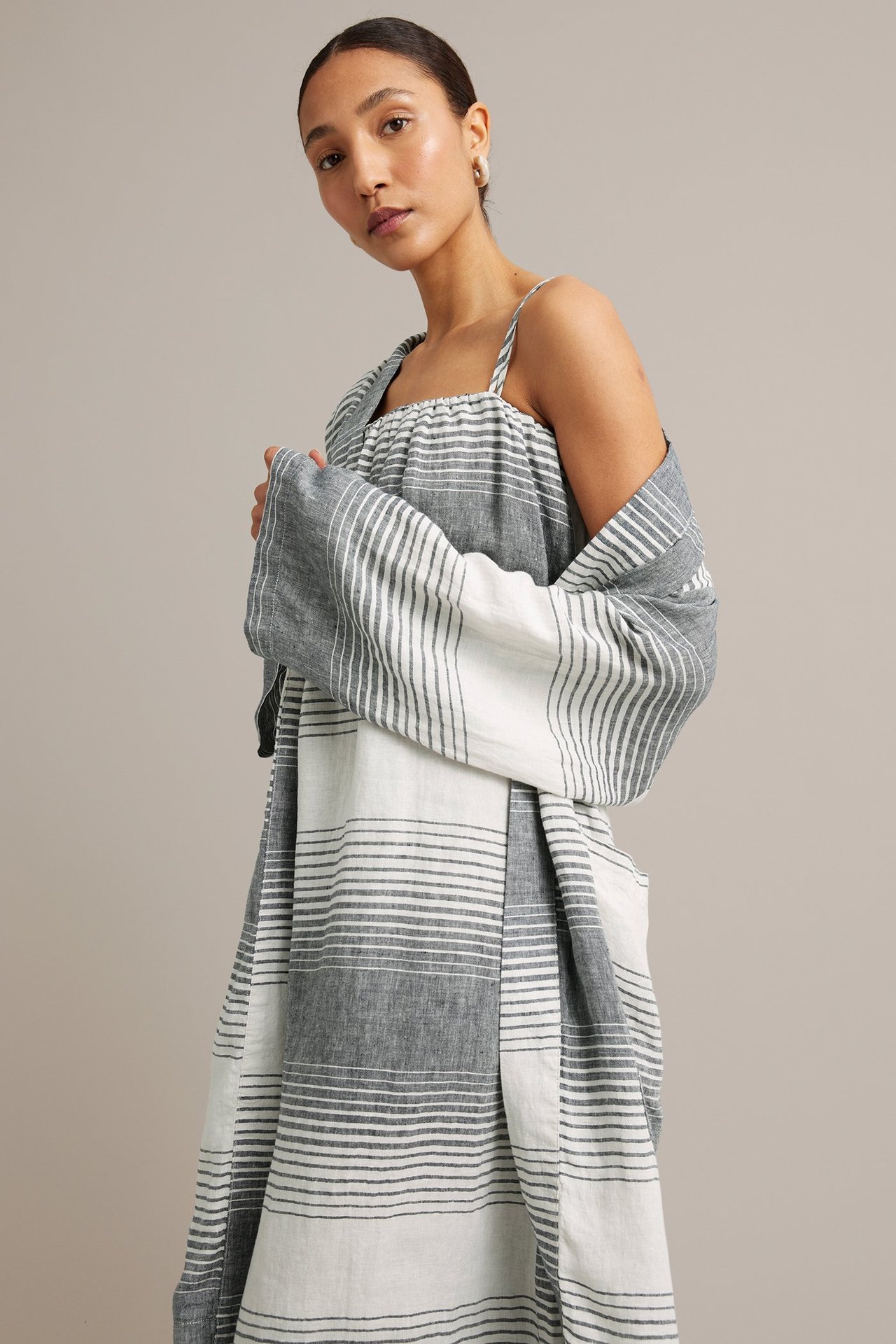 Kvinna i en mörkblå och vitrandig linneklänning med matchande knytskärp, framifrån.