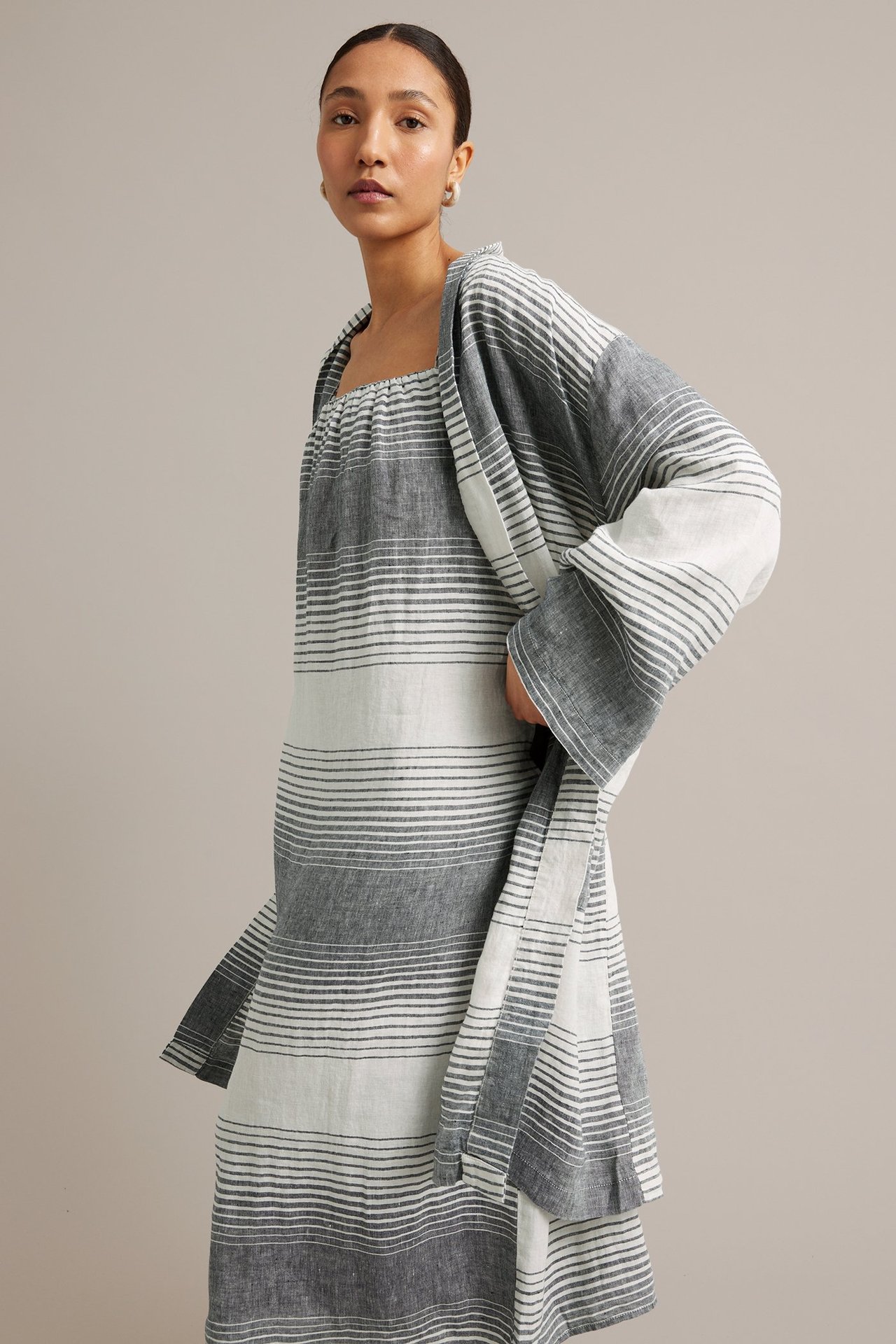 Frontvy av en kvinna i mörkblå-vit randig linnklänning med samlad halsringning och matchande öppen jacka.