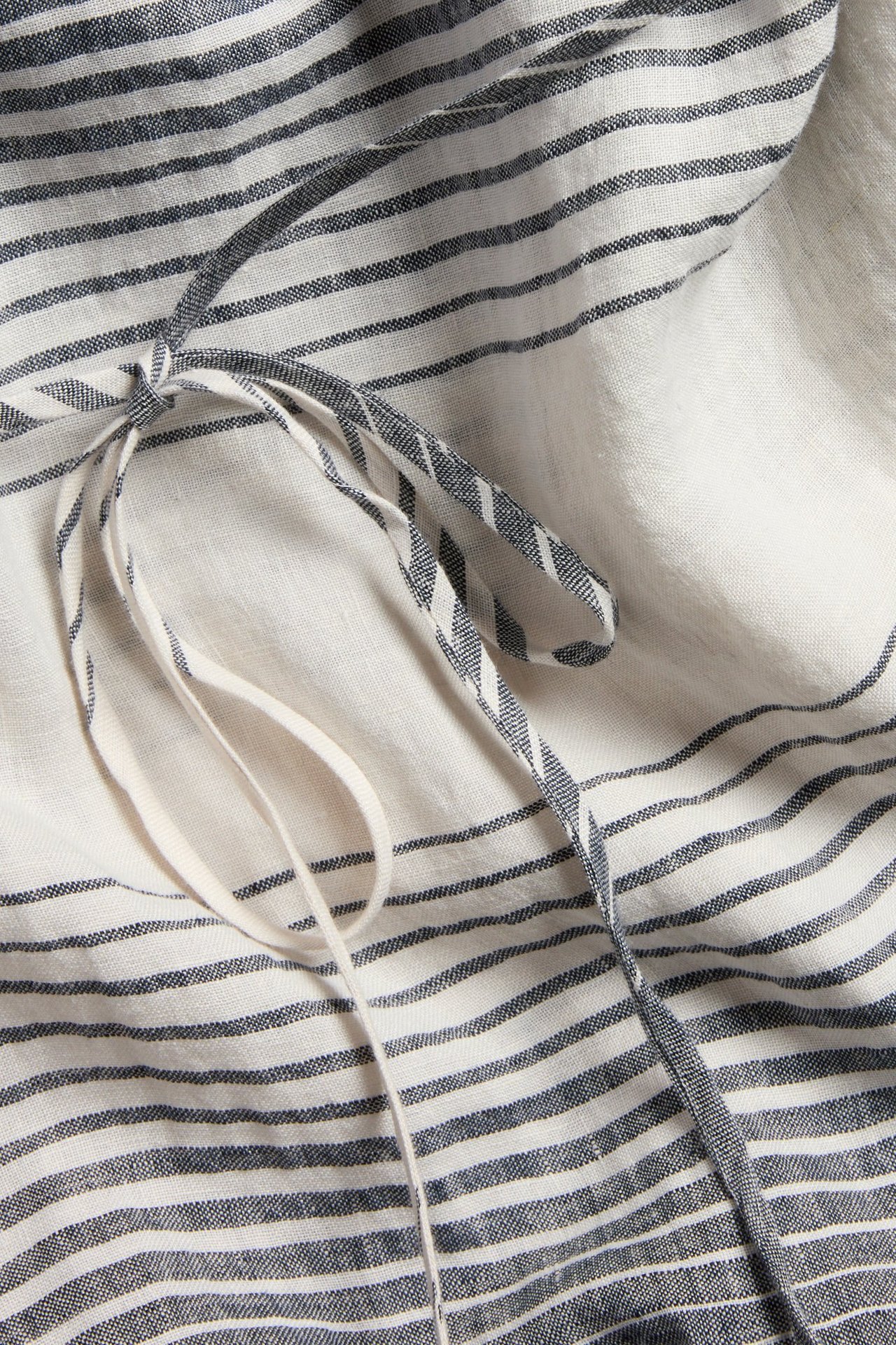 Lähikuva raidallisesta tummansinisestä pellavamekosta, sidotulla kangasvyöllä ja luonnonvalkoisella nauhalla.