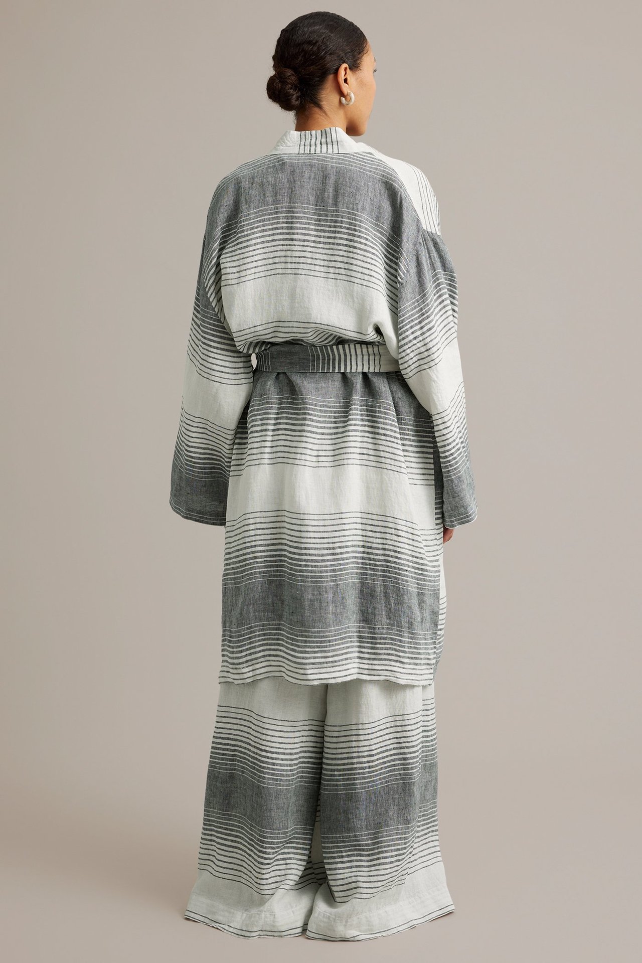 Ryggvy av en kvinna i en grå- och vitrandig linnekimono med knytskärp över matchande vida byxor.
